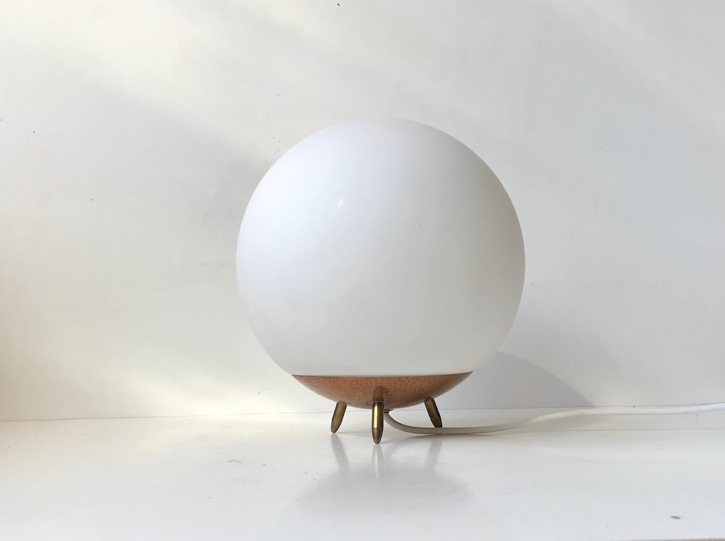 Unusual, small and yet voluminous table lamp composed of a stylized tripod hammered copper and brass base and a free-resting mat white opaline glass sphere. In Scandinavia we call this design a 'Space Bug'. It was manufactured in Scandinavia during
