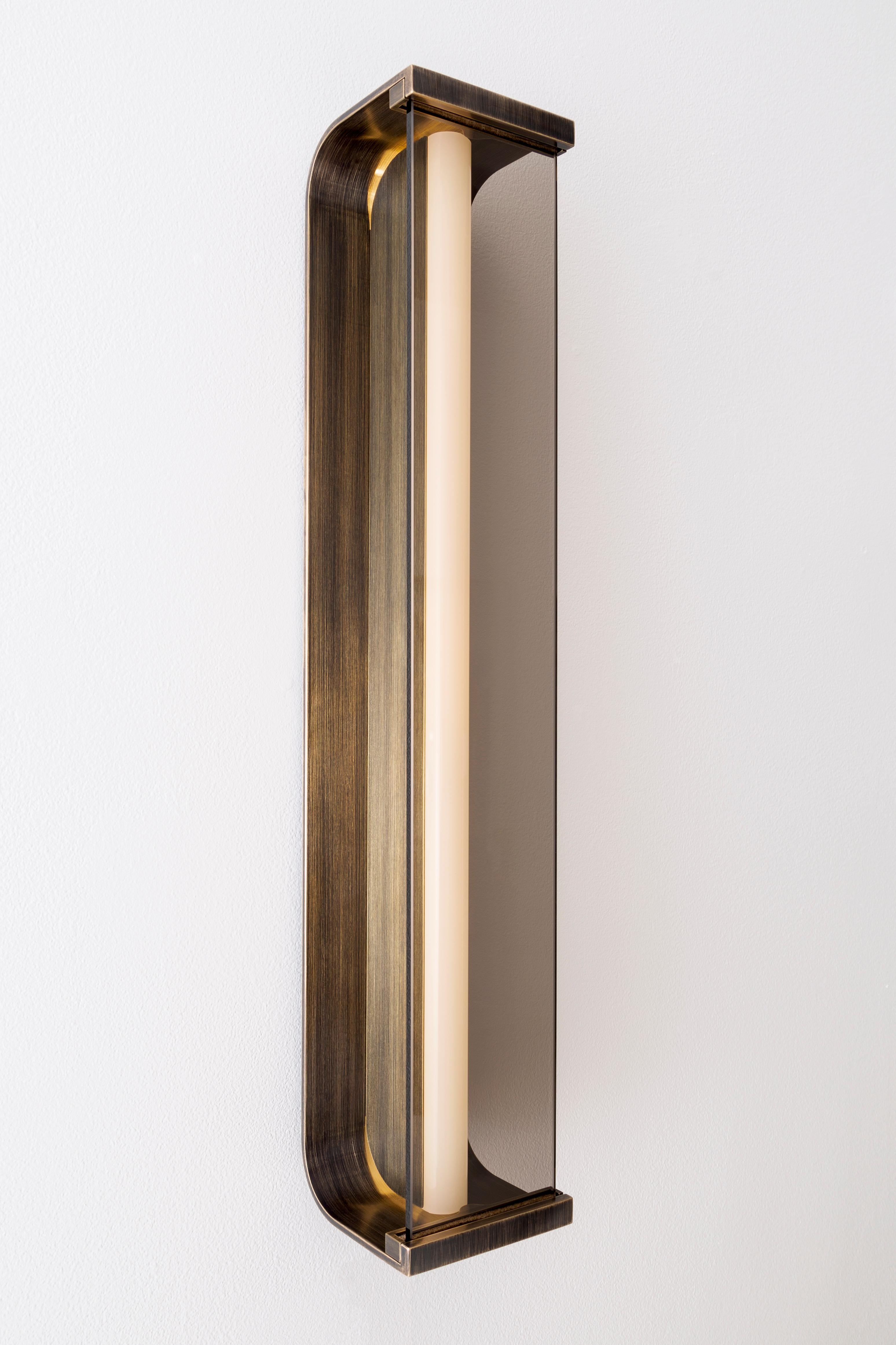 Spacek wall sconce features a minimal forged brass body that supports a linear glass lens. Light filters through bronze, smoke, or starphire glass. Fixture body is available in satin brass, antique brass or blackened Brass to coordinate with a range