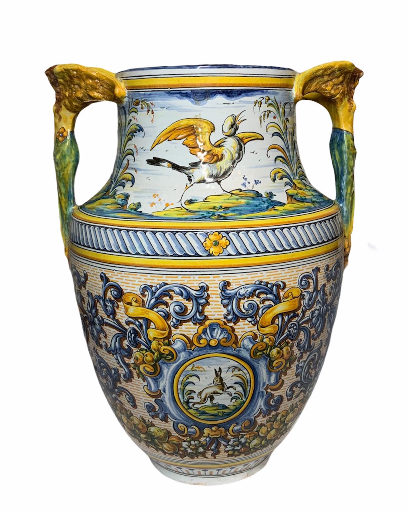 This is a polychromed large urn vase depicting a continuos scene of a running deer and a bird singing in the neck of it; while in the body side there are another continuous images of a bird trying to fly and a hare jumping. Both images are adorned