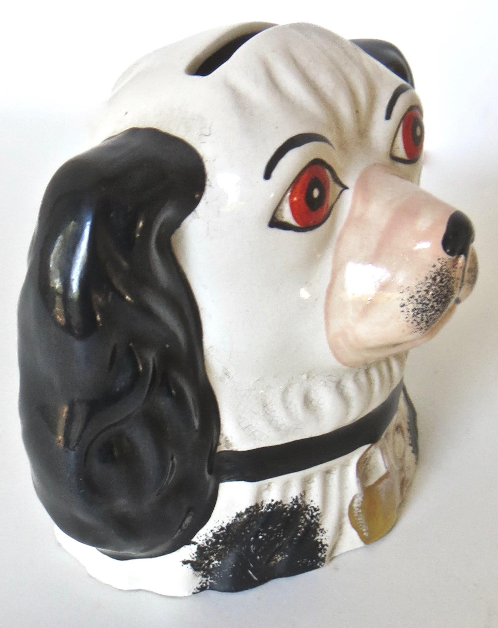 In the image of a Spaniel, this porcelain dog bust was utilized for putting used razor blades in the slot provided at the top and discarded when filled. It is quite attractive with rust/orange eyes, black ears and highlights, a padlock hanging from