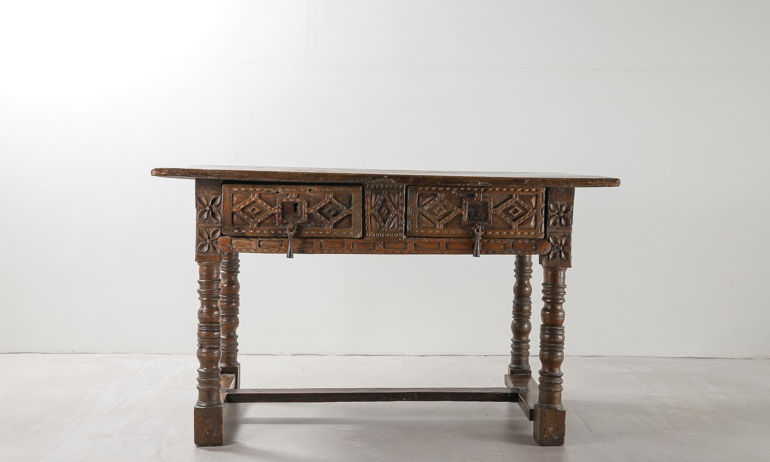 An ornately carved desk originating from Spain in the late 17th century. 

Heavy turned legs joined by stretchers, supporting a two drawer frieze with geometric and floral carved details to both the front and back of the piece. 

Two sturdy and