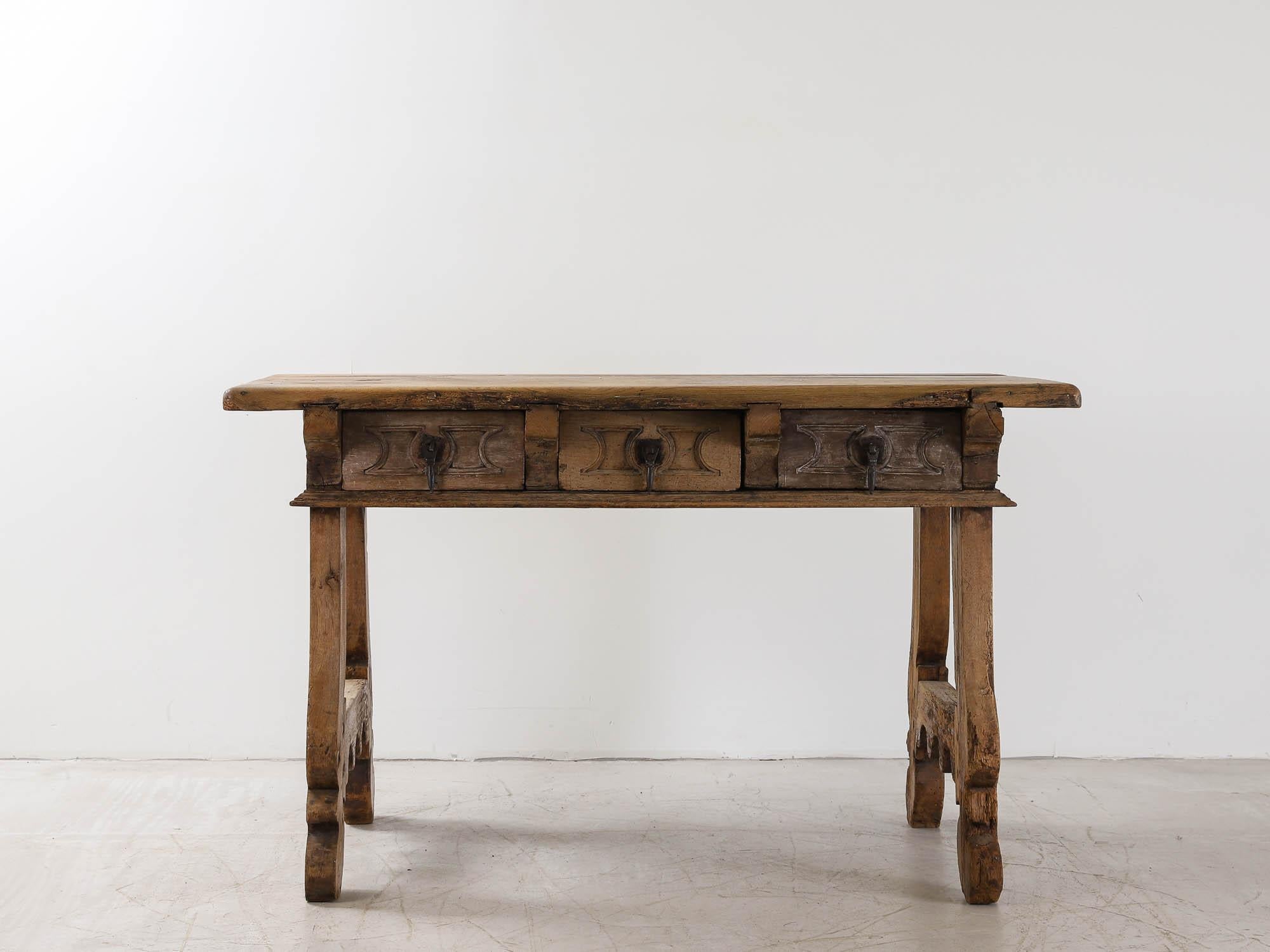 An 18th Century Spanish carved walnut table. With a thick, honey coloured, patinated top sitting on a three carved drawer frieze with original iron pulls, supported by trestle lyre legs.