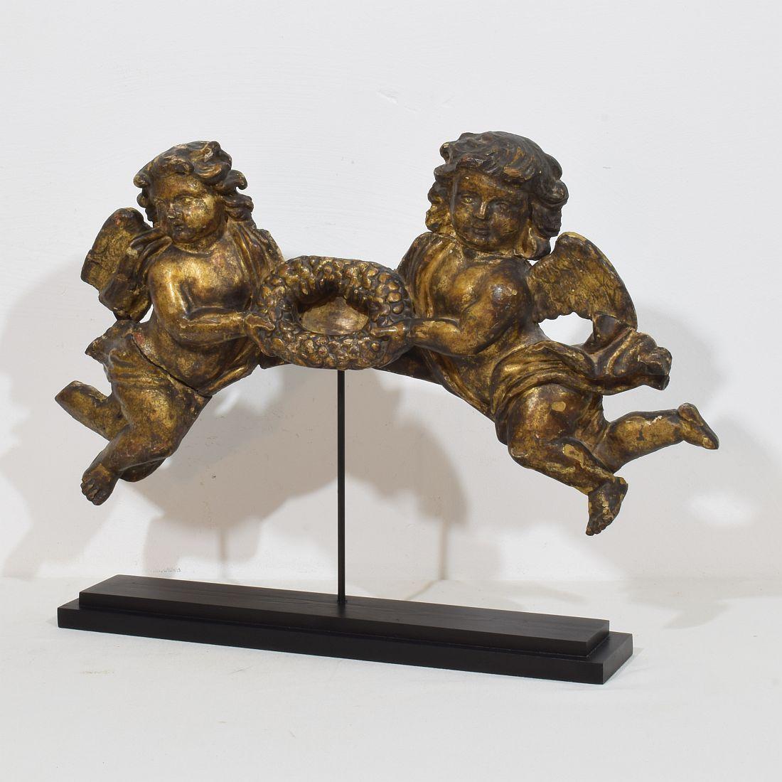 Bellissimo ornamento in legno intagliato a mano che raffigura due angeli che tengono una corona d'alloro. Un pezzo unico d'epoca.
Spagna, circa 1700-1750
Intemperie. Piccole perdite e vecchie riparazioni.

Le misure qui sotto includono la base in