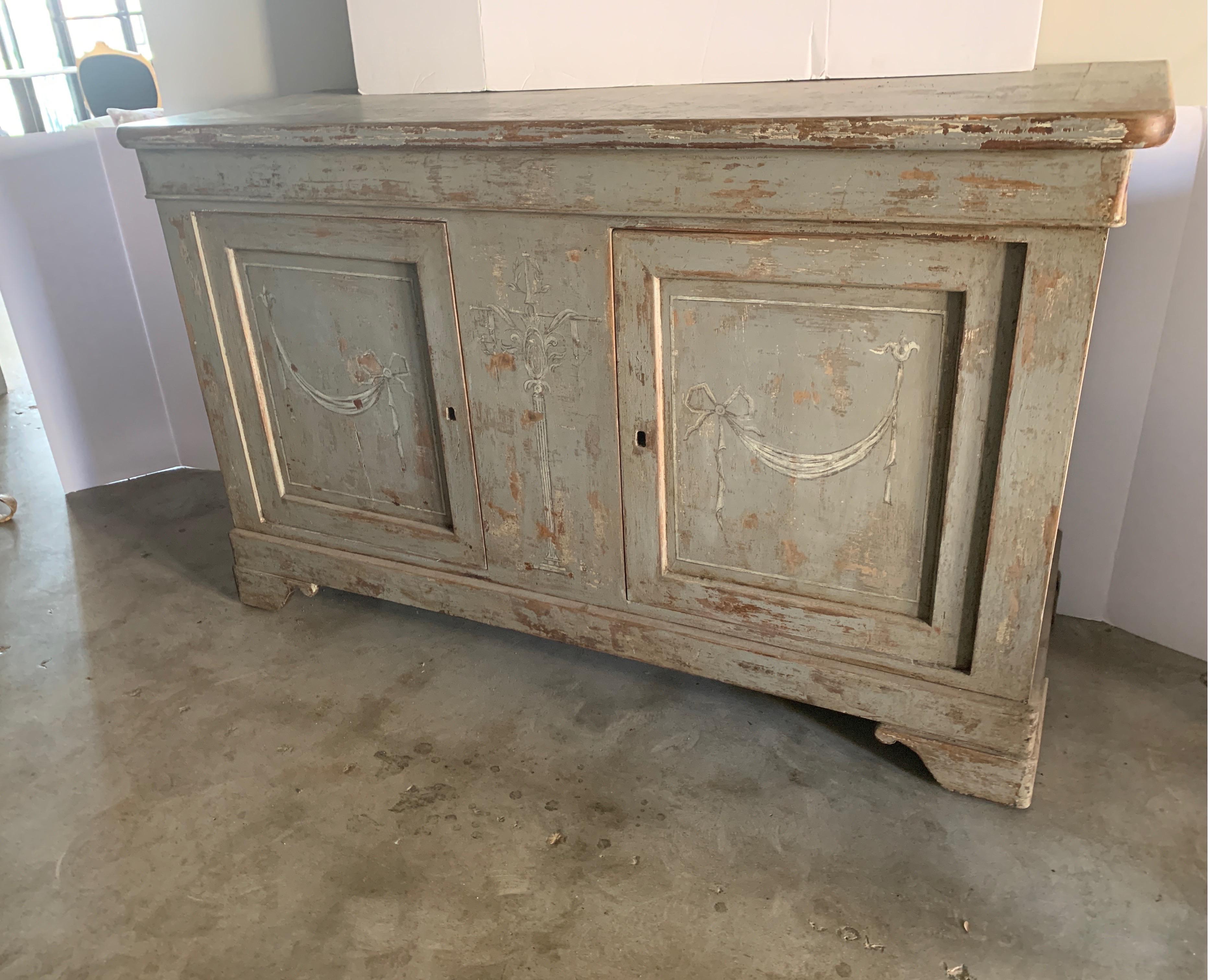 Spanish two door walnut buffet painted lates with medium gray paint and creamy motif with ribbon. It has a stationary center piece and middle and bottom shelf inside that goes all the was through, meaning the length side to side for storage.