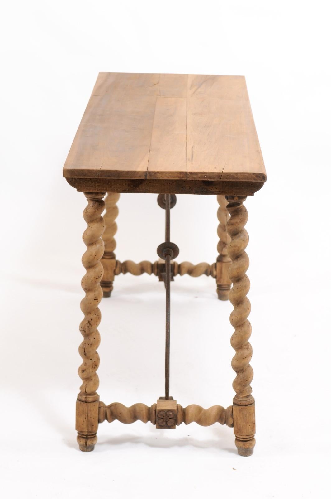 A Spanish Baroque style oak trestle console table from the early 20th century, with barley twist legs and decorative forged-iron stretcher. Born in Spain during the second decade of the 20th century, this exquisite console table features a