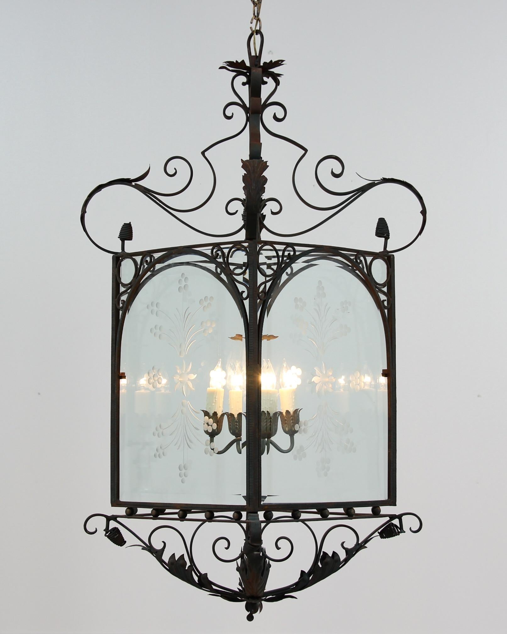 Monumental, 1930s pair of Spanish wrought iron lantern chandeliers in the Baroque style. These impressive lanterns feature painted iron frames with beveled glass panels. The dark green paint on the iron has naturally distressed and shows a beautiful
