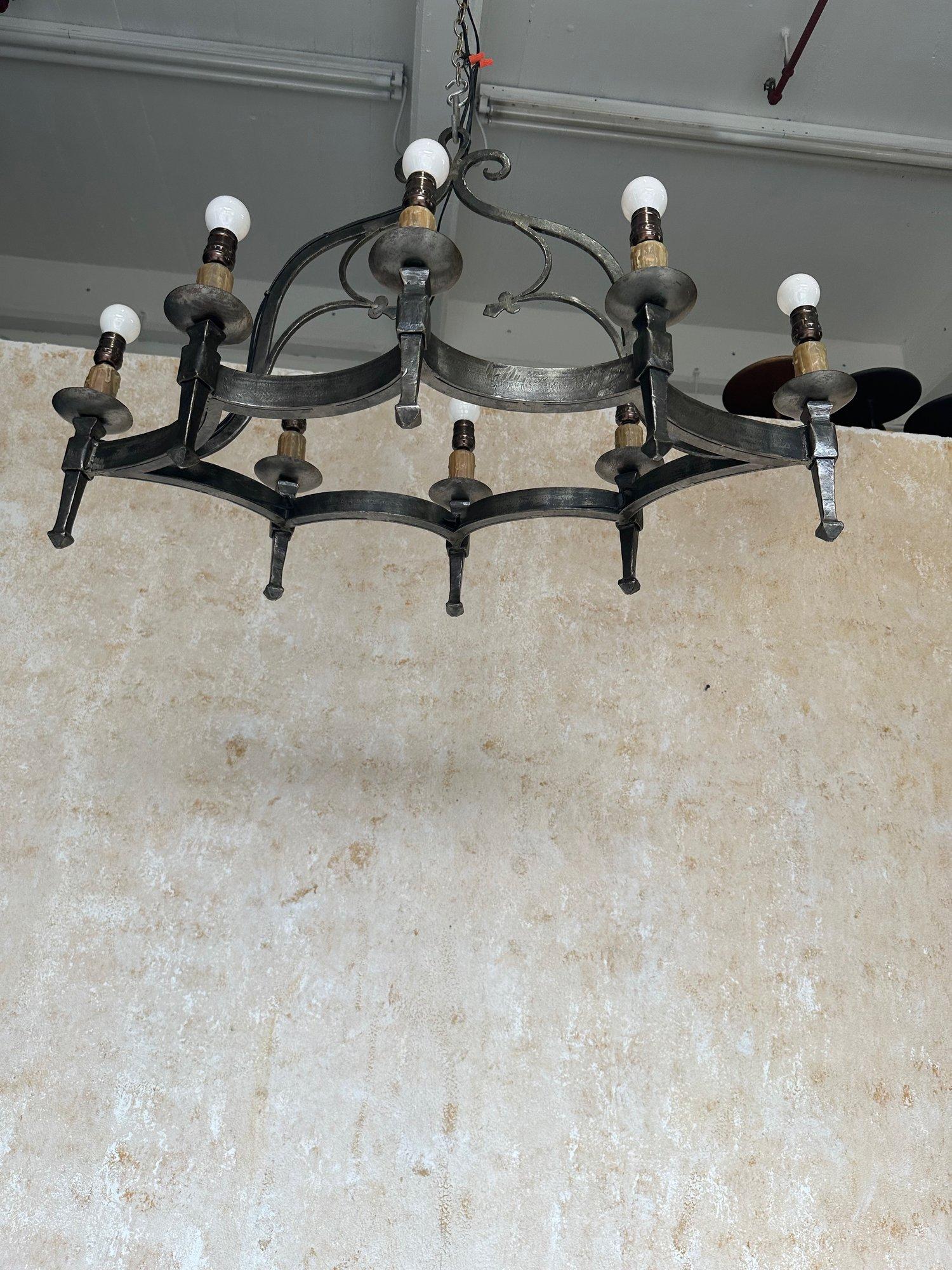 Questo insolito lampadario in ferro in stile medievale spagnolo degli anni '40 presenta una struttura robusta con otto bracci a torcia sospesi da una gruccia ornata. L'apparecchio è stato recentemente cablato per ospitare otto lampadine Edison,