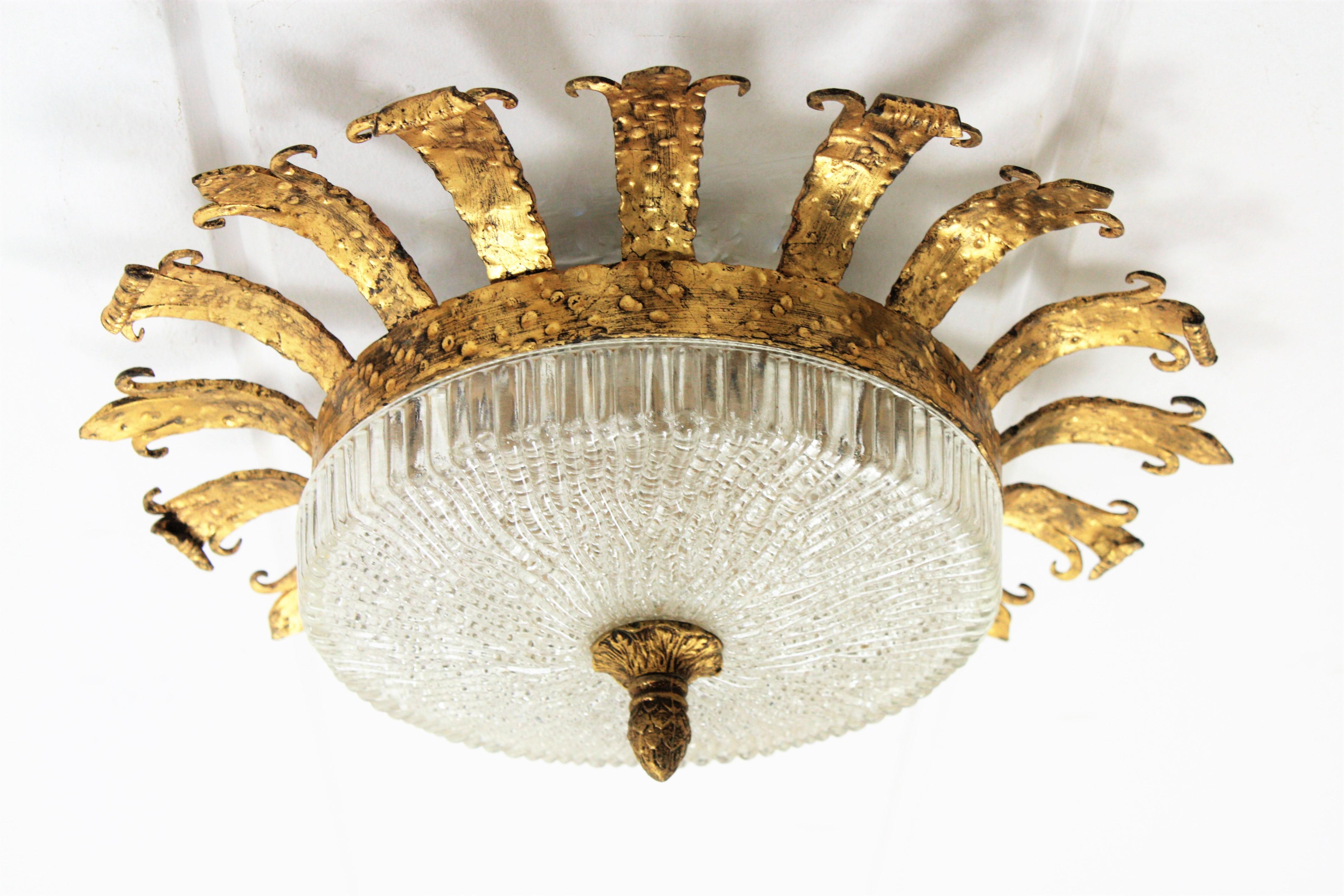 An sculptural hand-hammered iron and glass ceiling light fixture with neoclassical and Gothic Revival accents. A forged and gilded iron fixture with a fluted frosted glass shade with a gilt iron ornamented finial. This lamp has an highly decorative