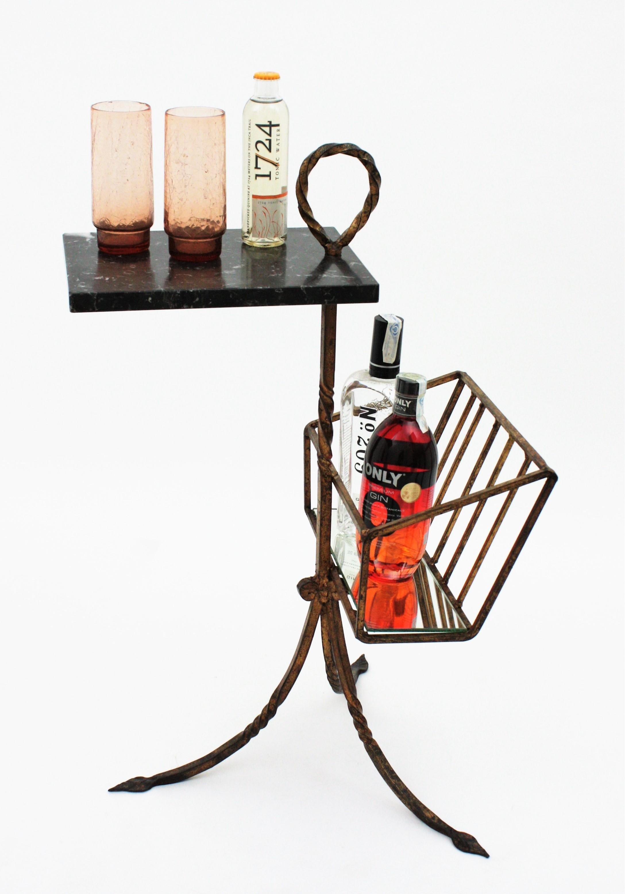 One of a kind gilt iron and black marble end table with magazine holder or drinks Stand. Spain, 1940s
This stylish hand forged iron table features a black marble tabletop standing on a git iron structure with a tripod base. The marble top has a