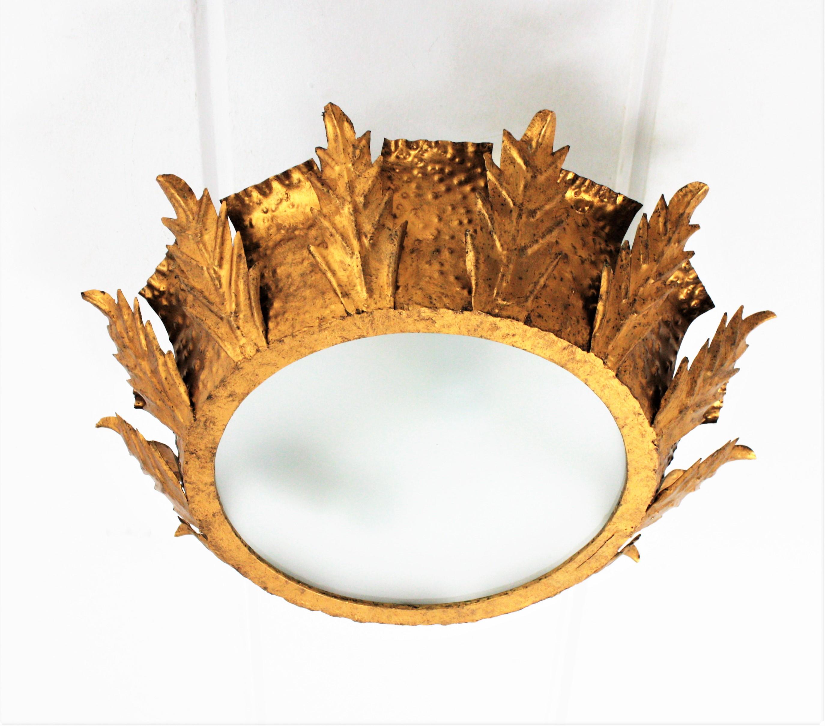 A hand-hammered medium sized sunburst crown shape leafed flush mount / pendant with frosted glass diffuser, Spain, 1950s.
The body of the light fixture is decorated by the hammer marks and hand-cut iron leaves. It has a nice gold leaf gilt aged