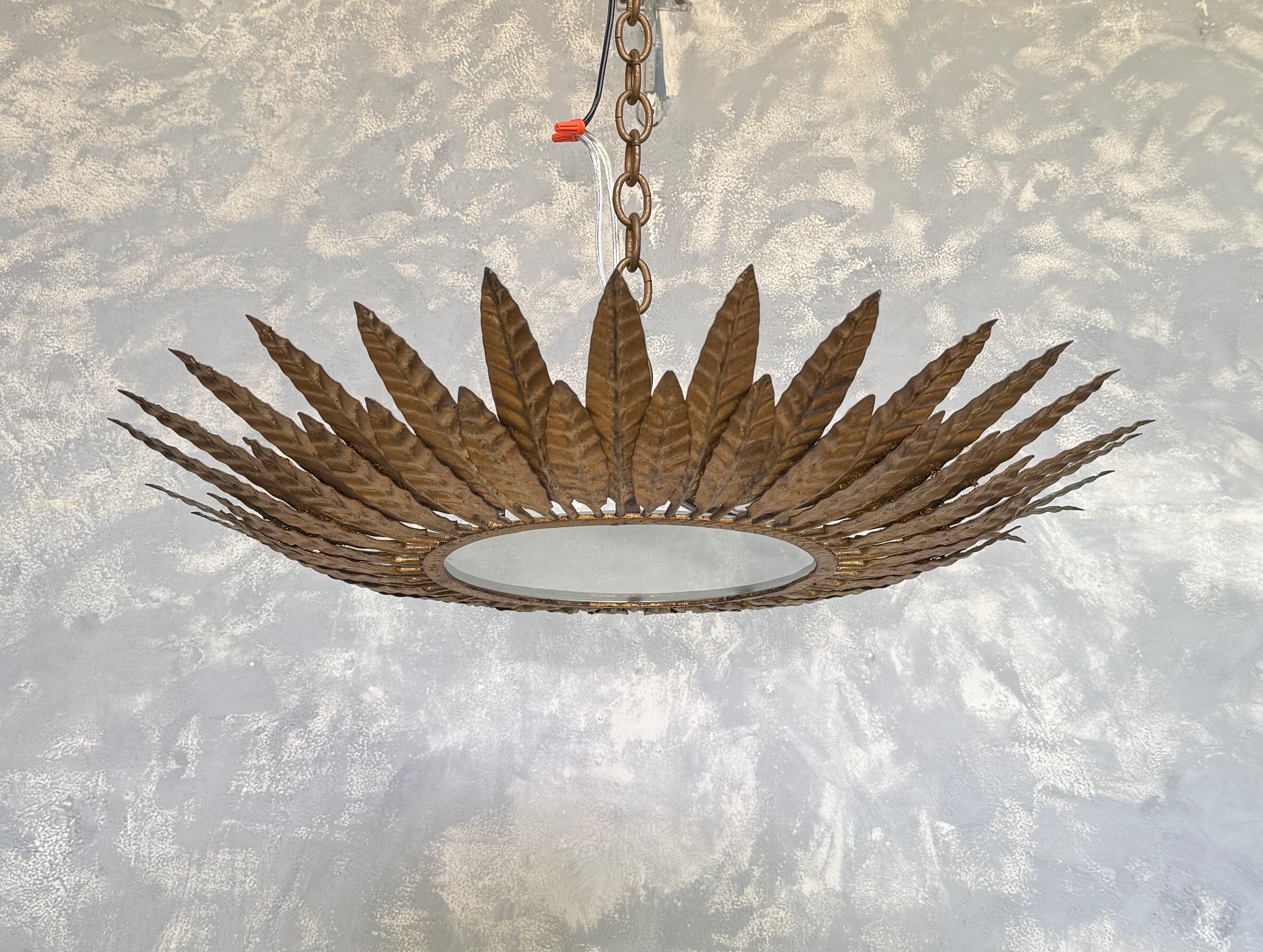 A striking 1950s Spanish gilt-metal flush-mount ceiling fixture featuring alternating rows of sculpted leaf motifs radiating from a central band. The hand-applied gold finish shows a beautifully aged patina, adding warmth and depth. Recently rewired