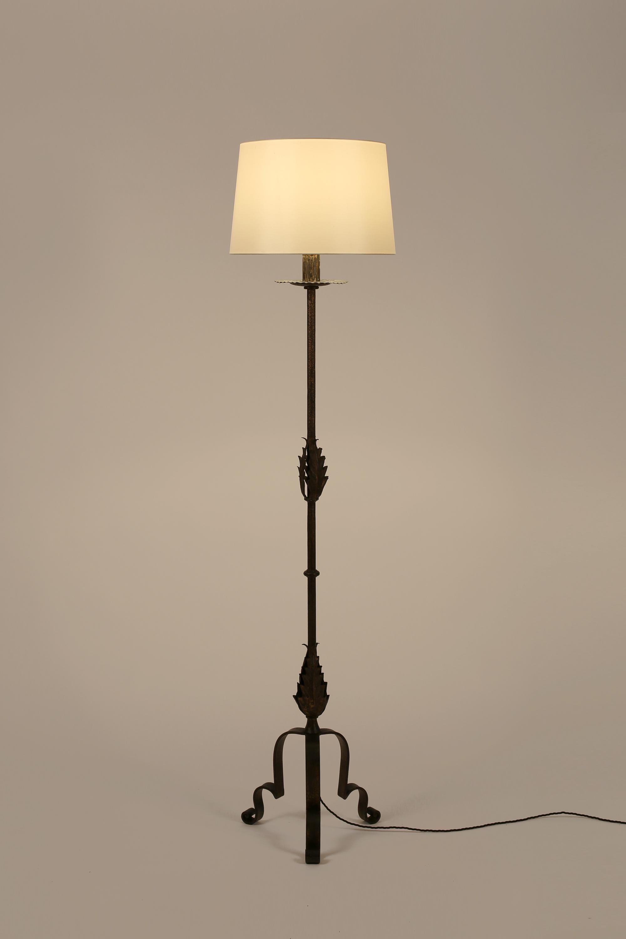 A forged and gilt iron floor lamp with ‘candle’ top, decorative foliate detailing to the stem and scrolling tripod base. Spanish, c. 1950s. Supplied with a tapered off-white dupion silk shade.

Rewired for the UK & PAT tested.