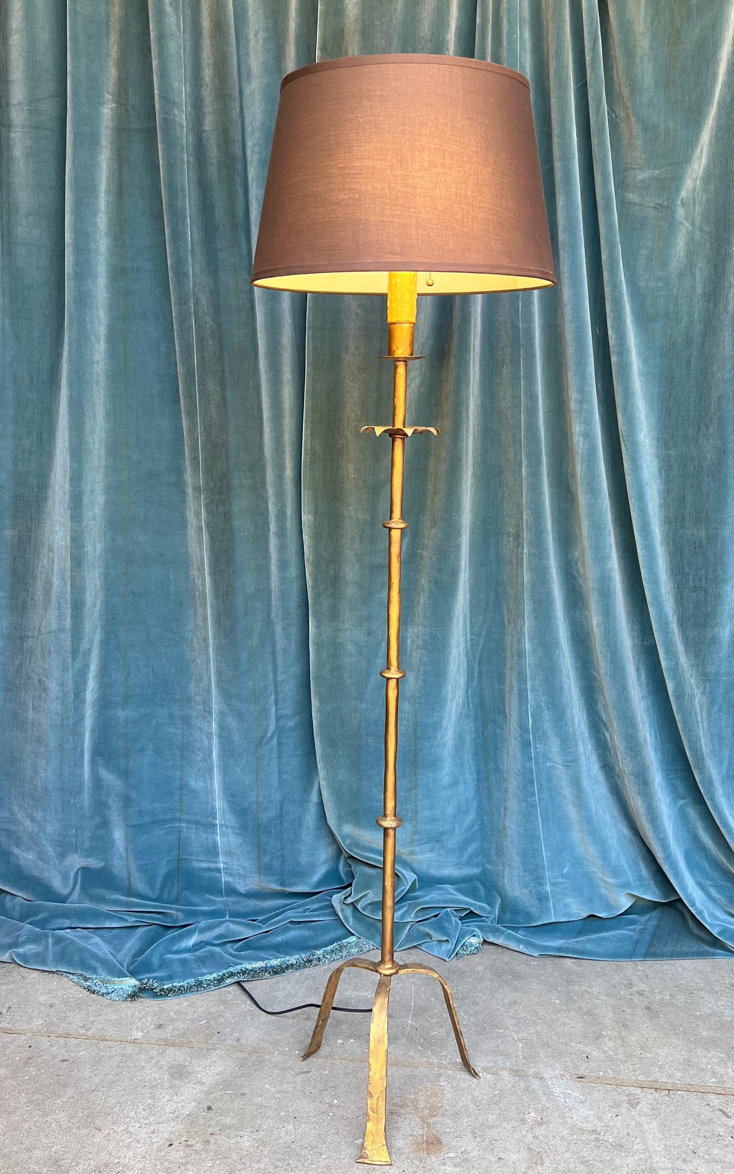 This Spanish 1950s wrought iron floor lamp is an embodiment of elegance and grace, perfect for illuminating any room. The elongated and raised tripod base, finished in a rich dark gilt patina, adds a sophisticated ambiance to the lamp. The stem of