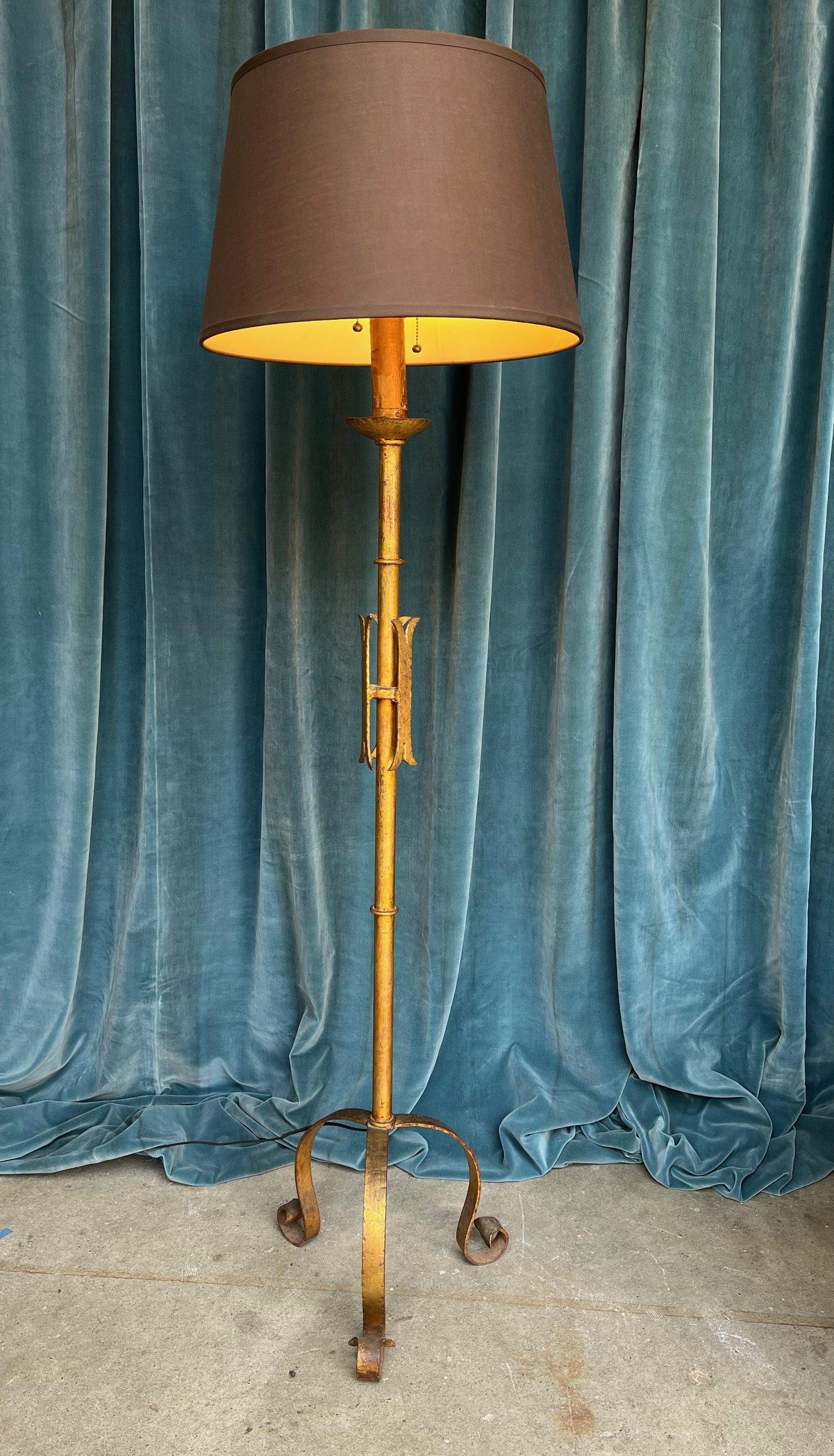Introducing a unique Spanish 1950s gilt iron floor lamp that adds a touch of elegance to any space. This iron floor lamp features a stunning gilt gold patina, creating a captivating visual appeal. The lamp's central stylized medieval motif showcases