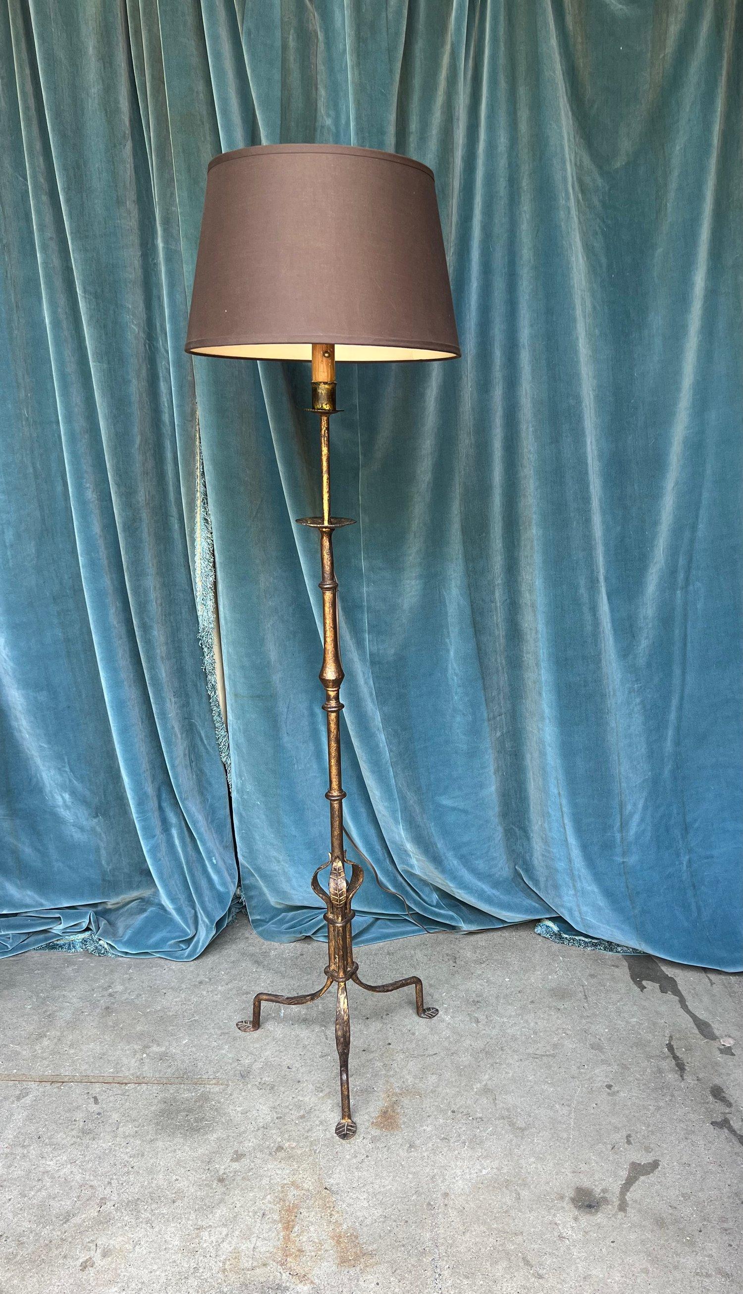 An unusual Spanish 1950s gilt iron floor lamp on an elevated tripod base. This remarkable and rare hand-wrought gilt iron floor lamp boasts intricate stylized motifs and an elevated tripod base. The dark gold patina, gracefully aged over time,