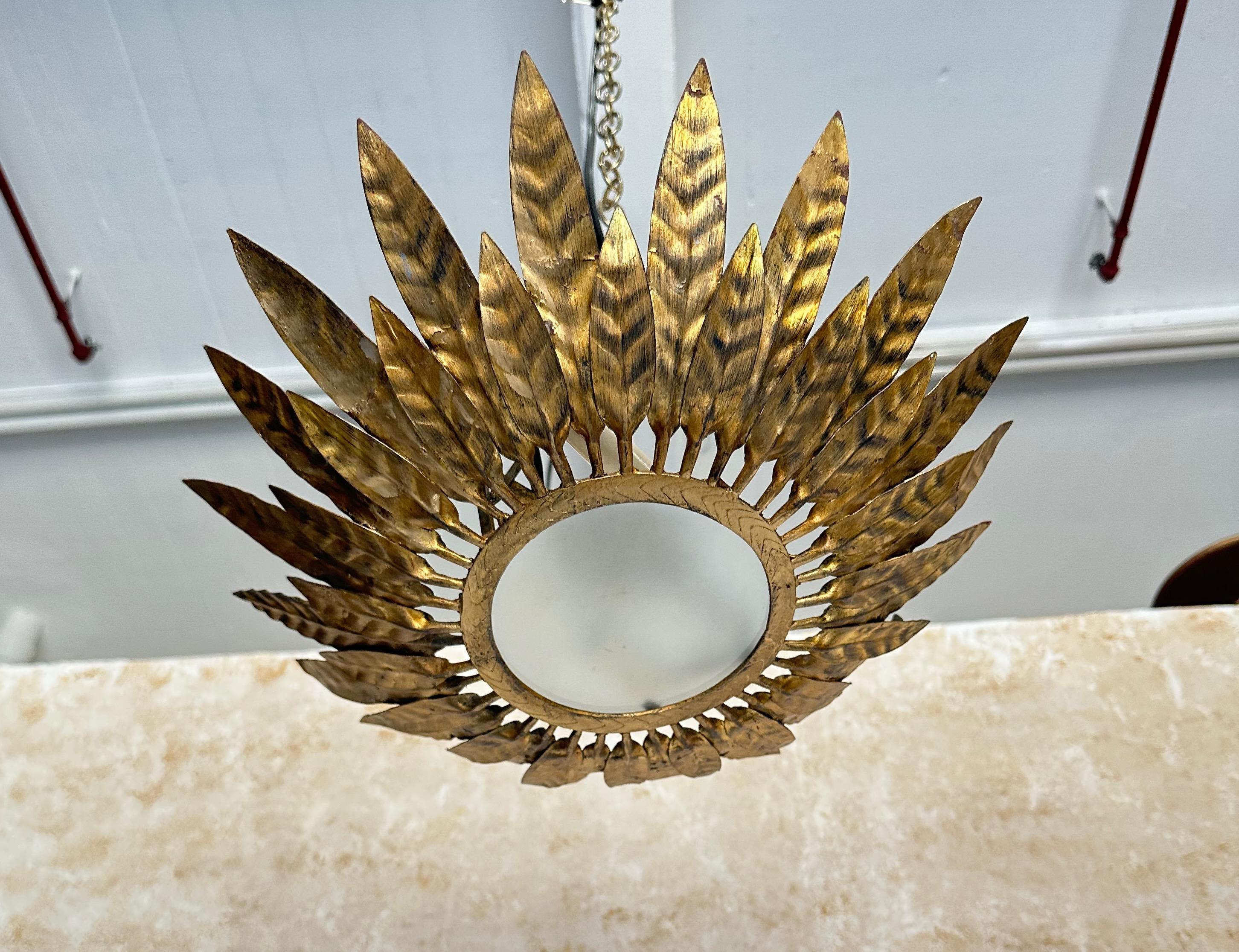 Cet élégant plafonnier espagnol vintage des années 1950 en métal doré présente une double couche de petites et grandes feuilles alternées et se chevauchant partiellement, rayonnant à partir d'un cadre circulaire robuste qui entoure le centre en