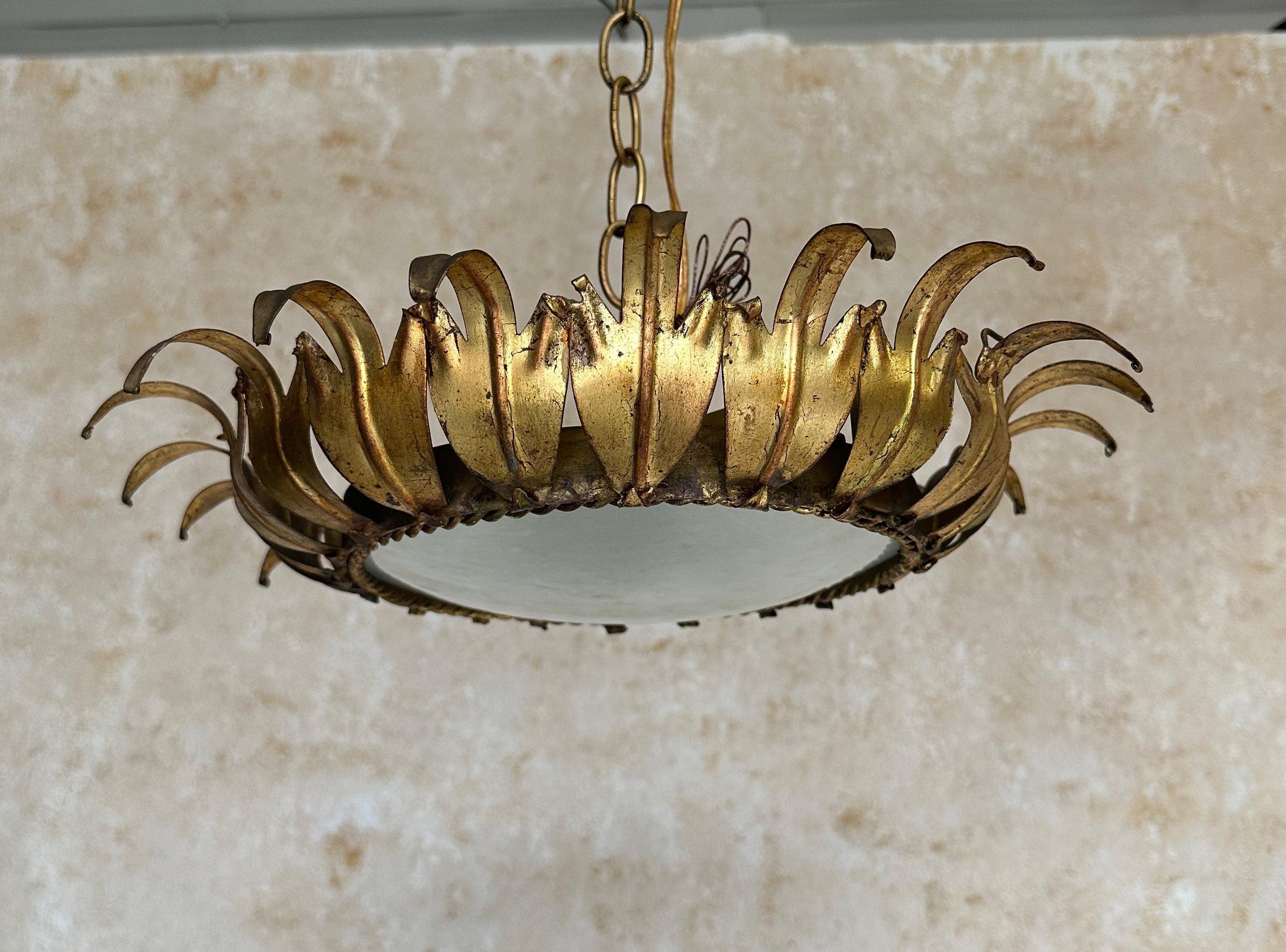 This stunning Spanish 1950s gilt metal ceiling fixture features an elegant crown of stylized gilt metal leaves surrounding a sturdy circular frame with a braided border that holds the convex frosted glass center. The rich gilt patina is original and