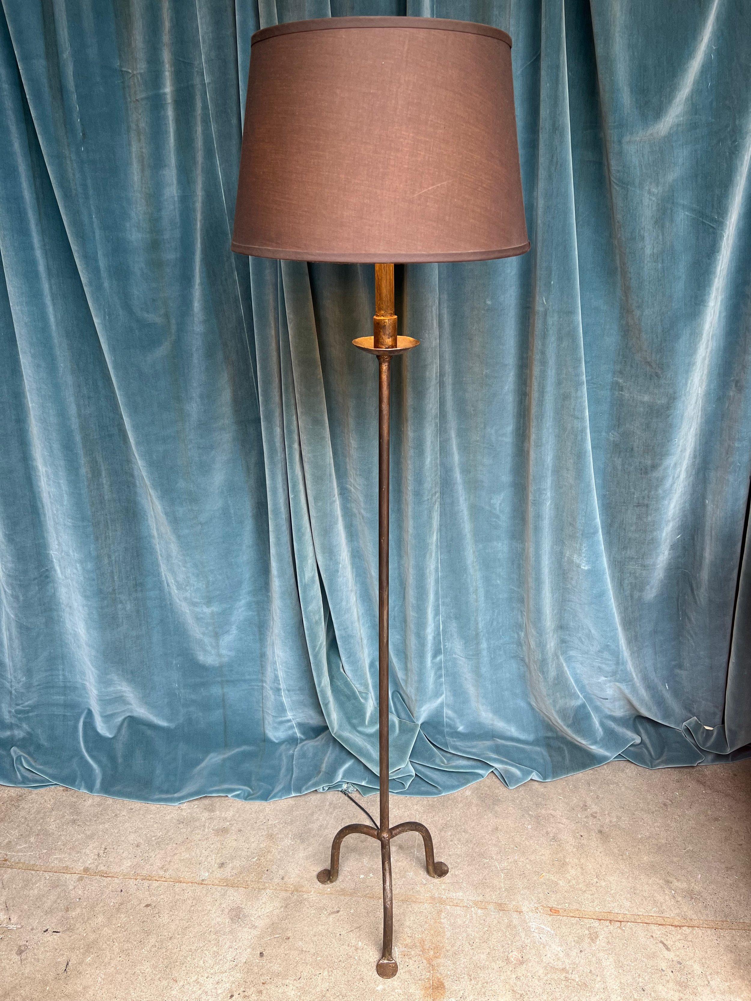 An exquisite Spanish 1950s wrought iron floor lamp, featuring a rounded tripod base with a rich, deep bronze patina that exudes elegance and sophistication. The bobeche supporting a hand-painted upper stem is a stunning detail that adds character