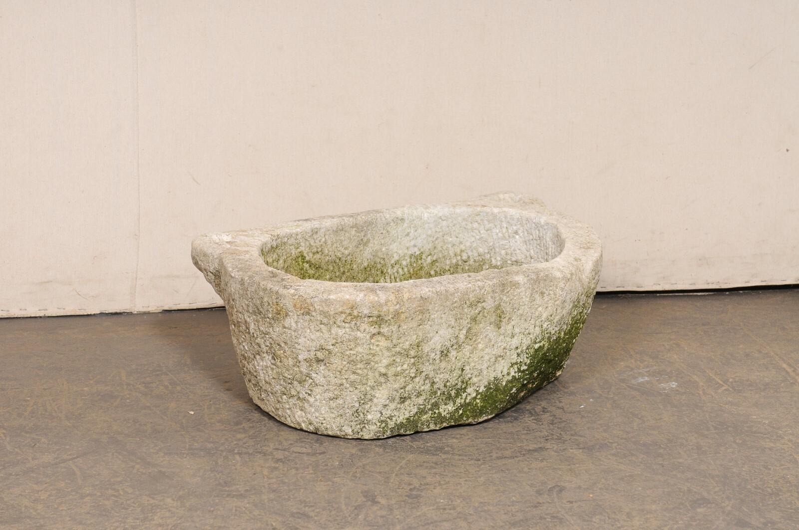 A Spanish hand-carved trough basin from the 19th century. This antique stone vessel from Spain has an oval-shaped basin with rounded front and flat backside, giving it an overall 