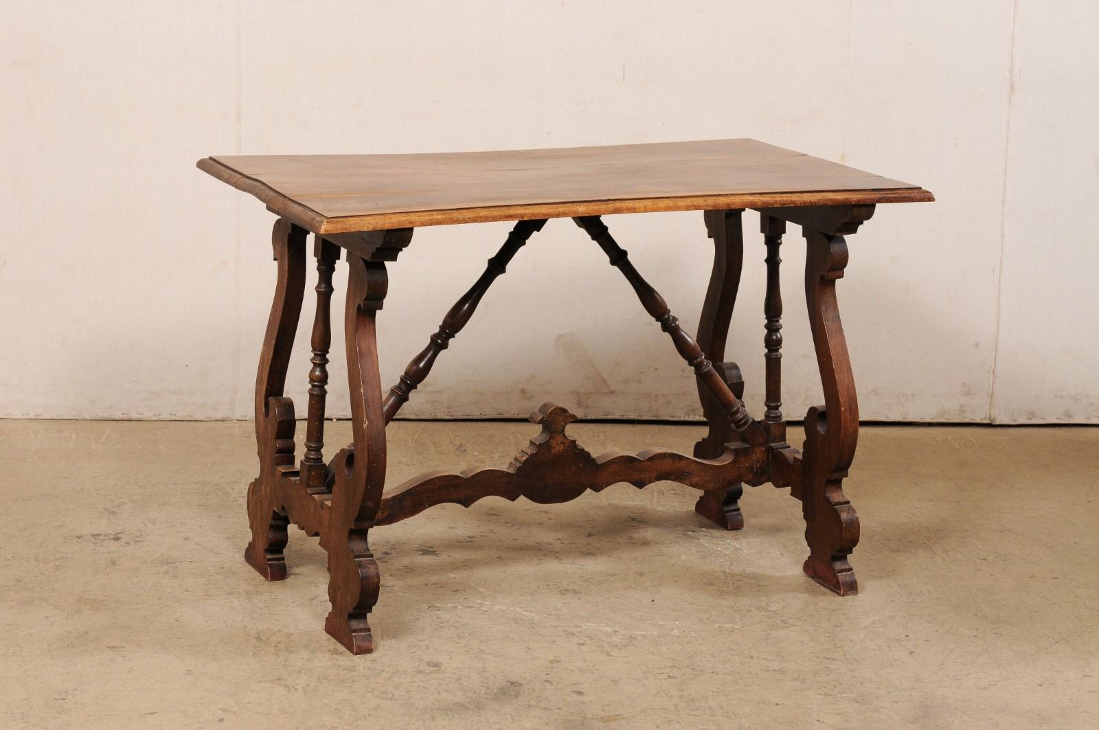 A Spanish walnut wood table with lyre legs from the 19th century. This antique table from Spain features a rectangular-shaped top which is raised upon a pair of sinuously carved trestle legs in a lyre design. The legs each have a spindle-carved post