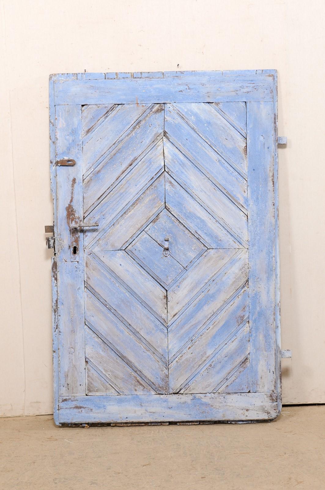 A Spanish painted wood door (which would make a great headboard) from the 19th century. This antique door from Spain has a diamond pattern front facing facade, created from boards, and central diamond has a forged iron hook- perhaps originally used