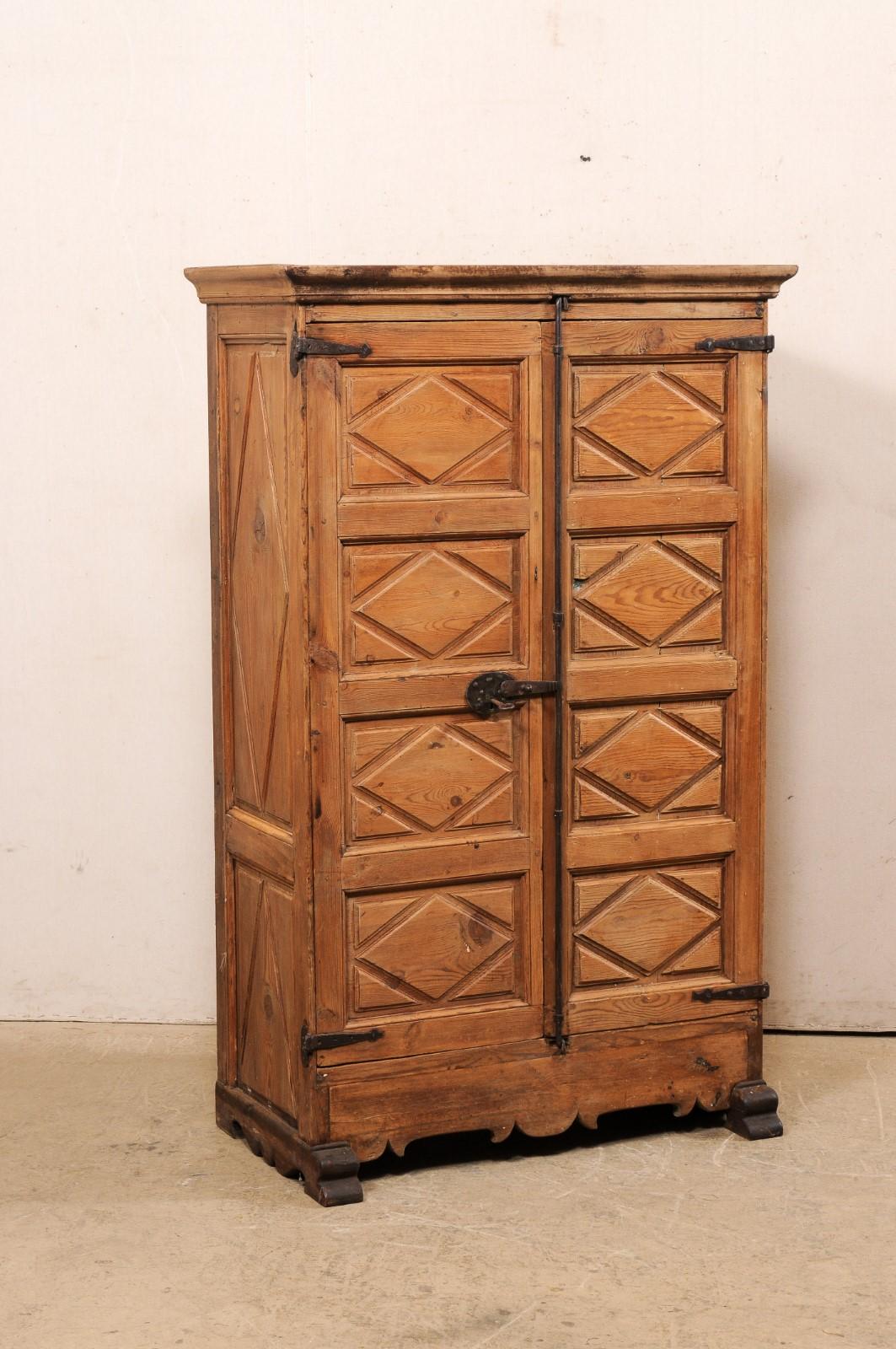 A Spanish carved-wood tall cabinet with two doors from the 19th century. This antique armoire from Spain features a molded cornice at top, with a case that houses a pair of four panel front doors which have been decoratively carved with a diamond
