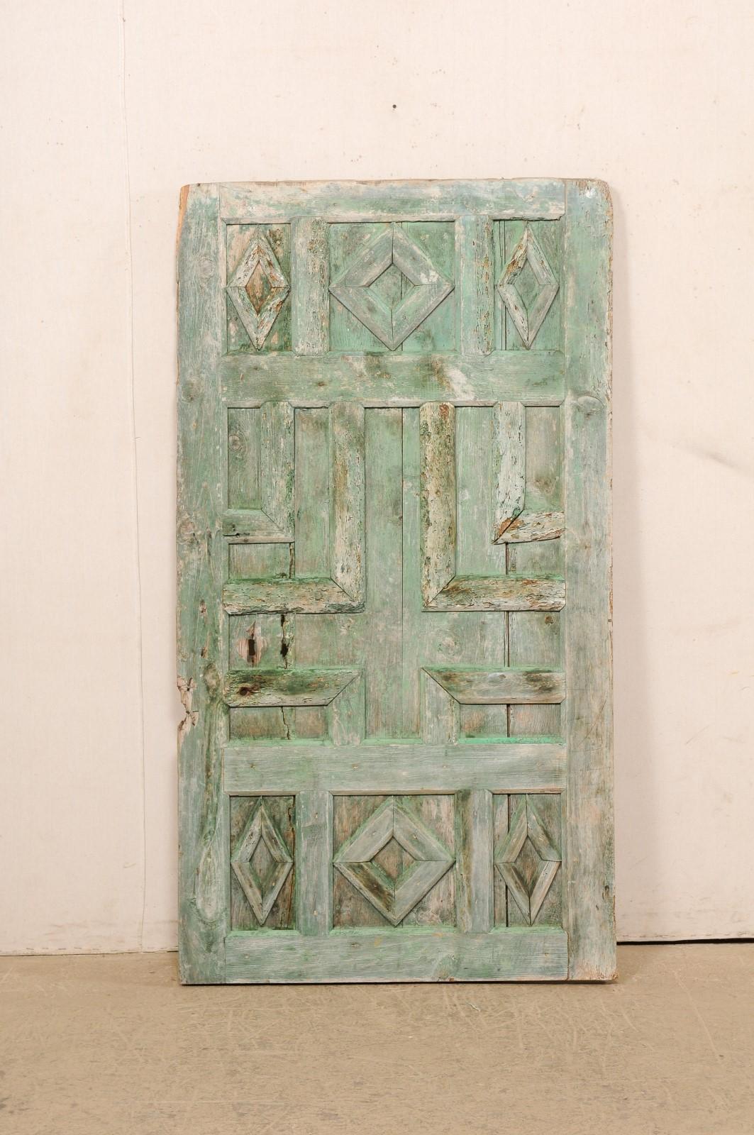 A Spanish painted decoratively paneled wood door from the 19th century. This antique door from Spain has been designed with raised panels; in various geometric designs, creating a unique and pleasing pattern. The front / decorated side retains its