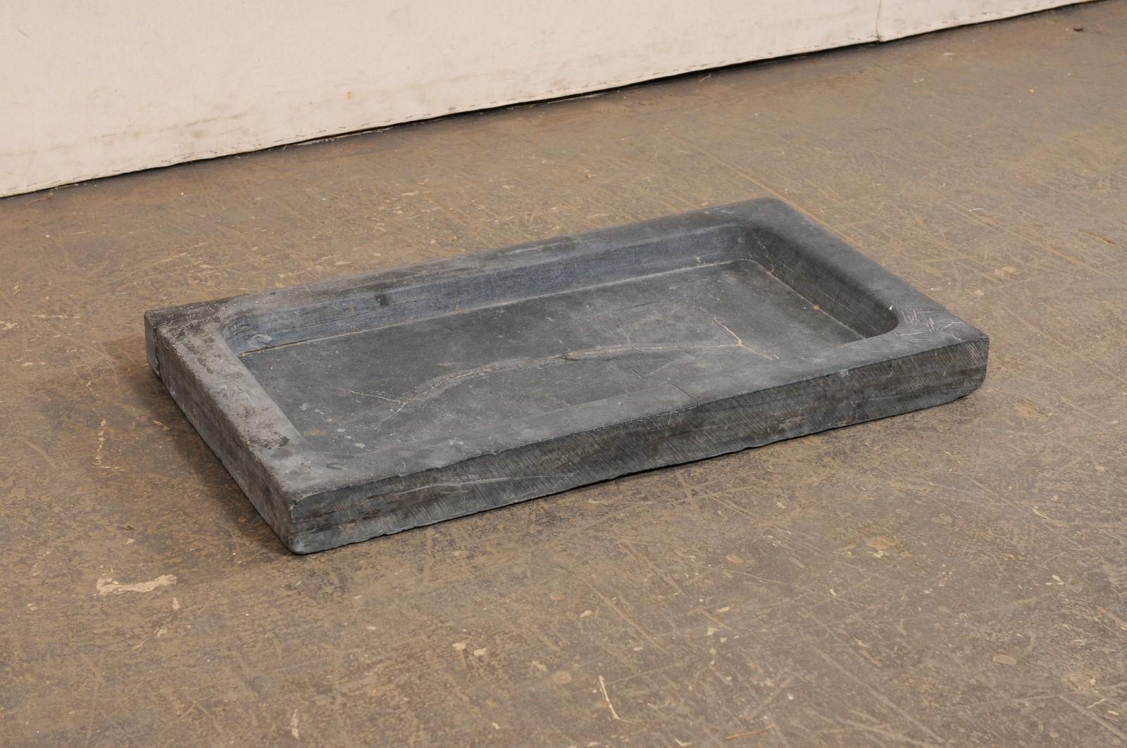 A Spanish carved-stone sink, with shallow basin and off-set drain hole, from the 19th century. This antique hand-carved grey stone sink from Spain has clean/simple lines, and an overall rectangular-shape, which houses a shallow, 2.5