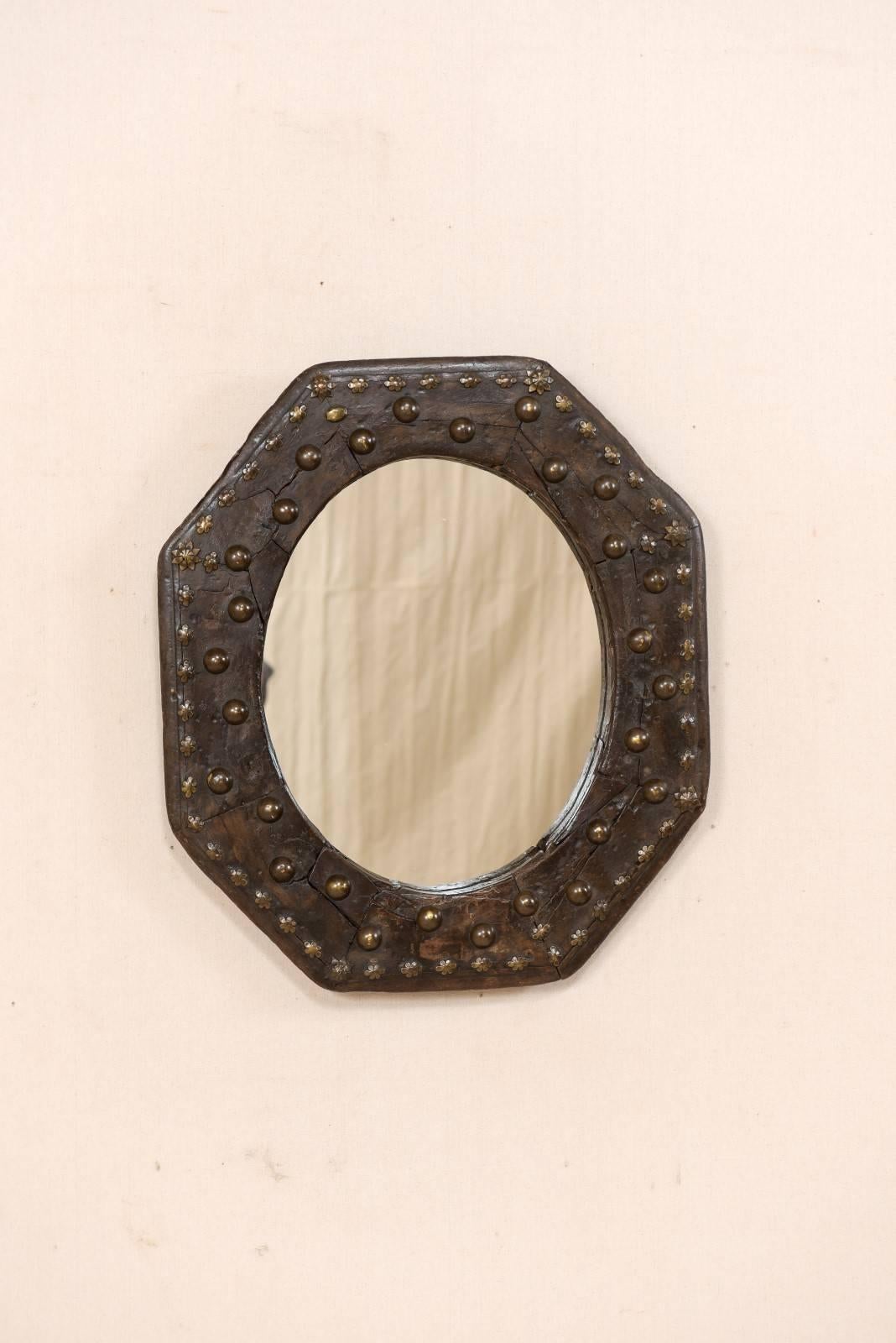 A Spanish 19th century octagonal wooden mirror. This handsome antique mirror from Spain features an octagon shaped wood surround, adorn with undulating round metal accents and smaller metal flowers about it's boarder edges. The brass accents are