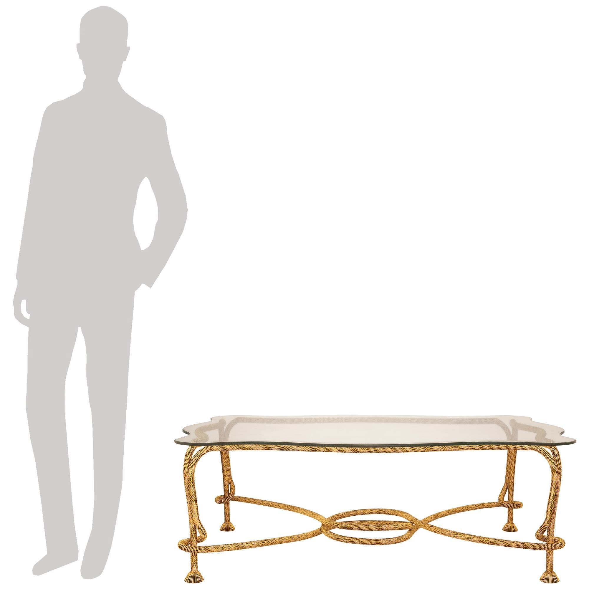 A unique and well known Spanish 20th century Gilt Metal and Glass coffee table by Emilio Rey, circa 1960s. This attention grabbing coffee table is designed with a Gilt Metal base and was made to look like tasselled rope with undulating curves along