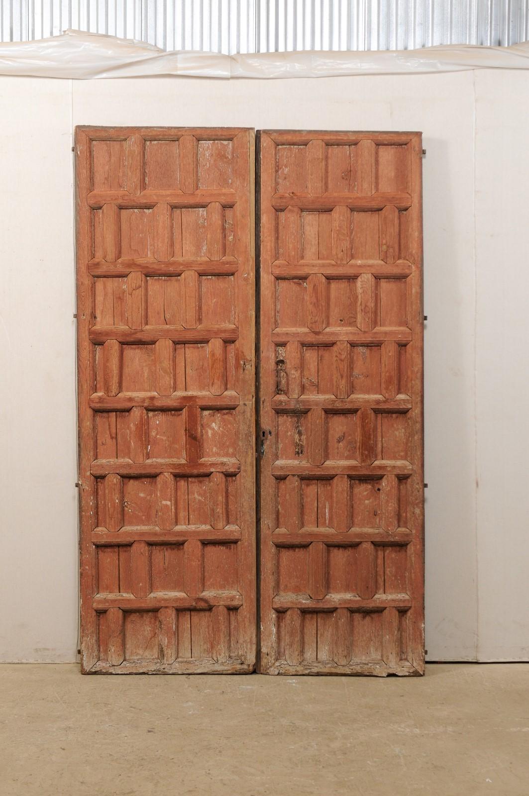 A Spanish pair of tall decoratively paneled doors from the turn of the 18th and 19th century. This antique pair of doors from Spain have been designed with thickly carved rows of staggered rectangular panels throughout their fronts sides, and have