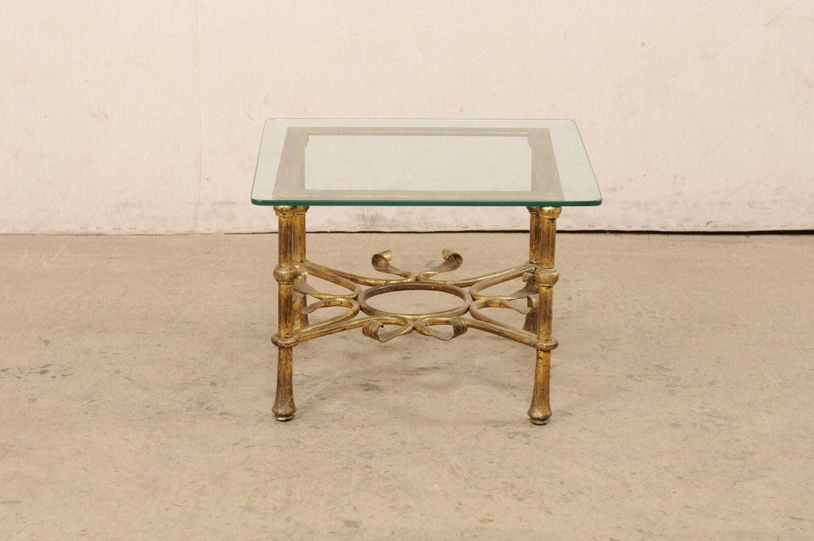 A Spanish small-sized coffee table with glass top from the mid 20th century. This vintage table from Spain features a square-shaped glass top, which is raised upon a metal frame comprised of a square top and four rounded legs at each corner, braced