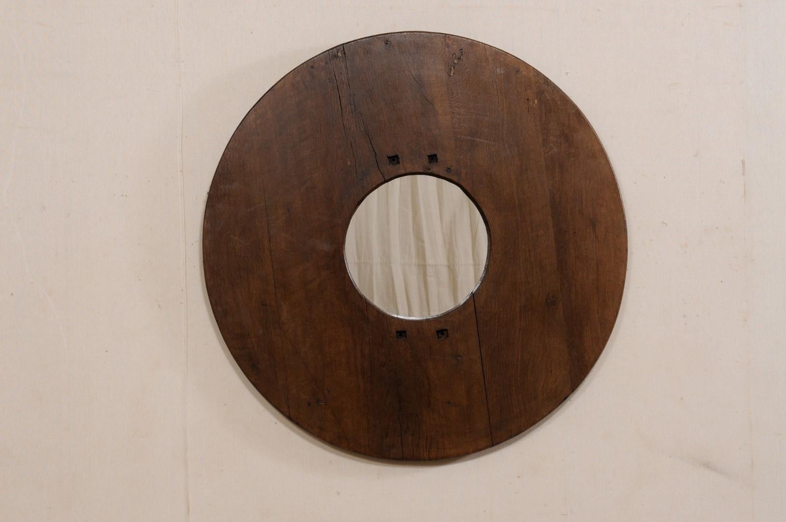 A unique circular mirror which has been custom fashioned with an antique Spanish wooden brazier as the surround, with new mirrored glass in it's center. This wall decoration features a new, circular-shaped mirror at center, within a beautiful wooden