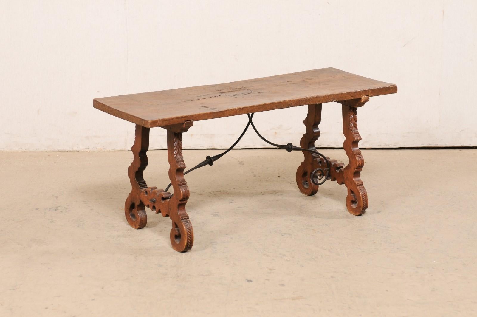 A Spanish wooden coffee table, with lyre legs and iron stretcher, from the turn of the 19th and 20th century. This antique table from Spain features a single-board rectangular-shaped top, which is raised upon a pair of sinuously carved lyre-legs
