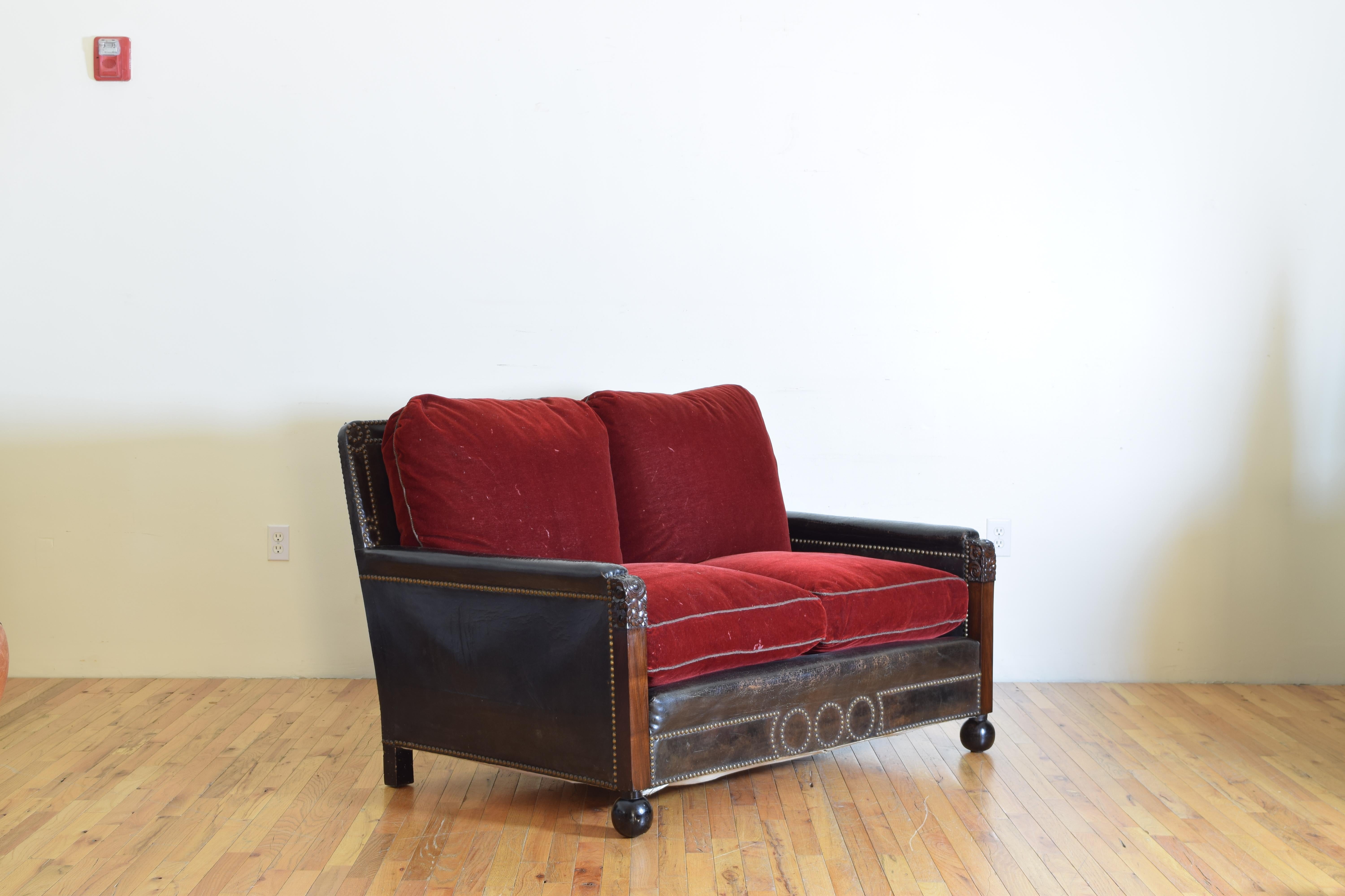 Having generous depth with four down filled cushions, the frame completely covered in leather with patinated nailhead trim, the frame raised on ebonized bun feet, second quarter of the 20th century.