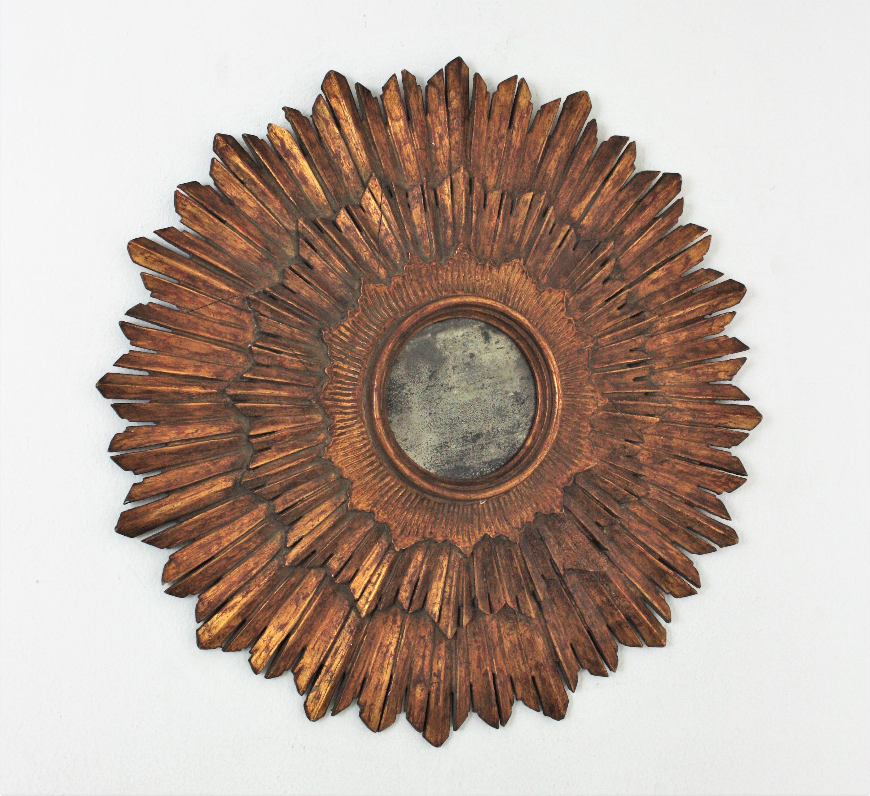Triple Layered carved wood sunburst mirror, Spain, 1930s.
The three layers of rays surounding the central round glass highlight its beauty. 
This wall mirror has a terrific aged patina showing its original gold leaf gilding and wearing its antique