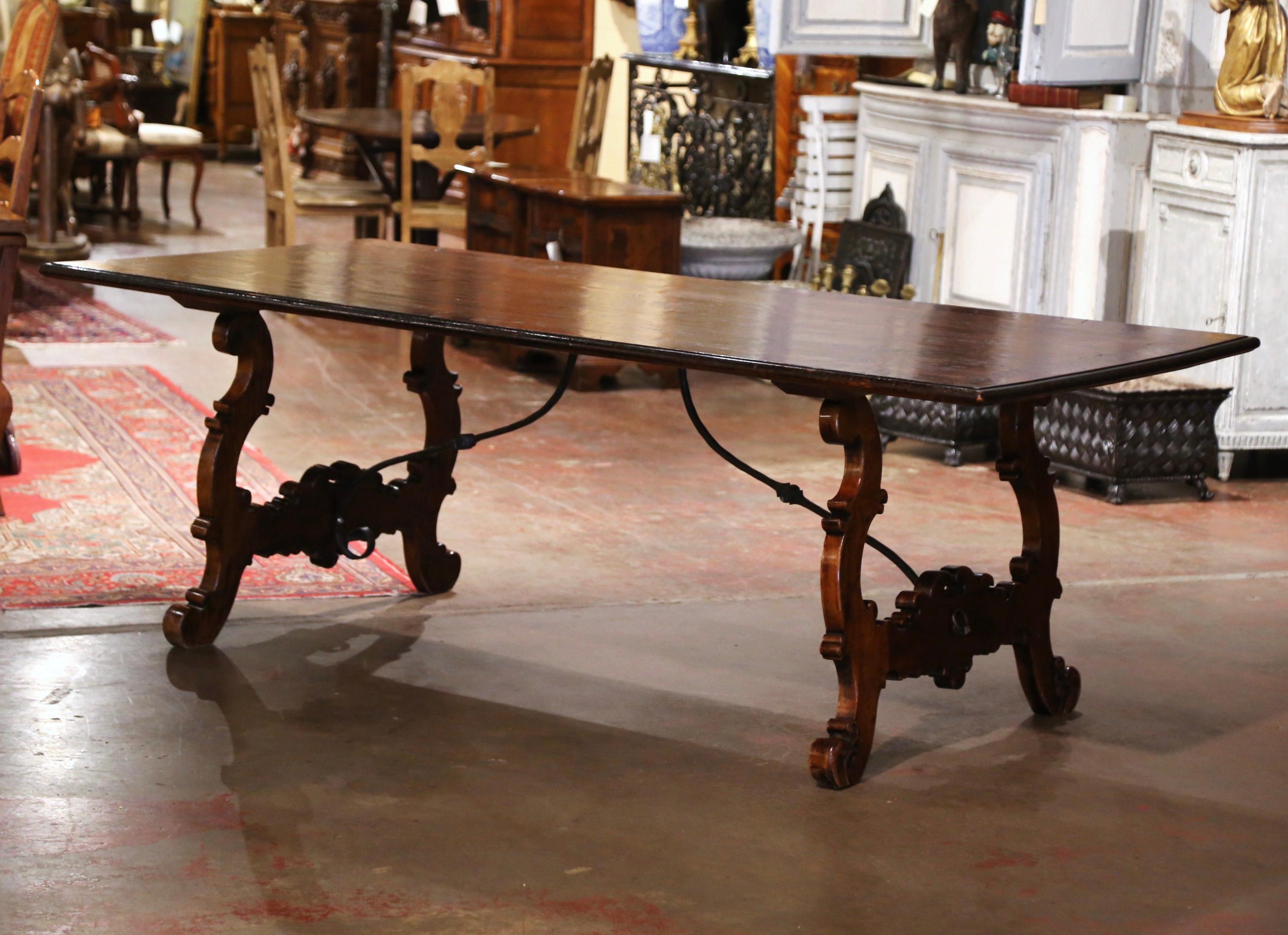 Decorate a dining or breakfast room with this elegant and large antique Spanish table. Carved in Spain circa 1980 and over 7 feet long, the trestle table stands on carved ox yoke leg supports, joined together with a thick scrolled forged double iron