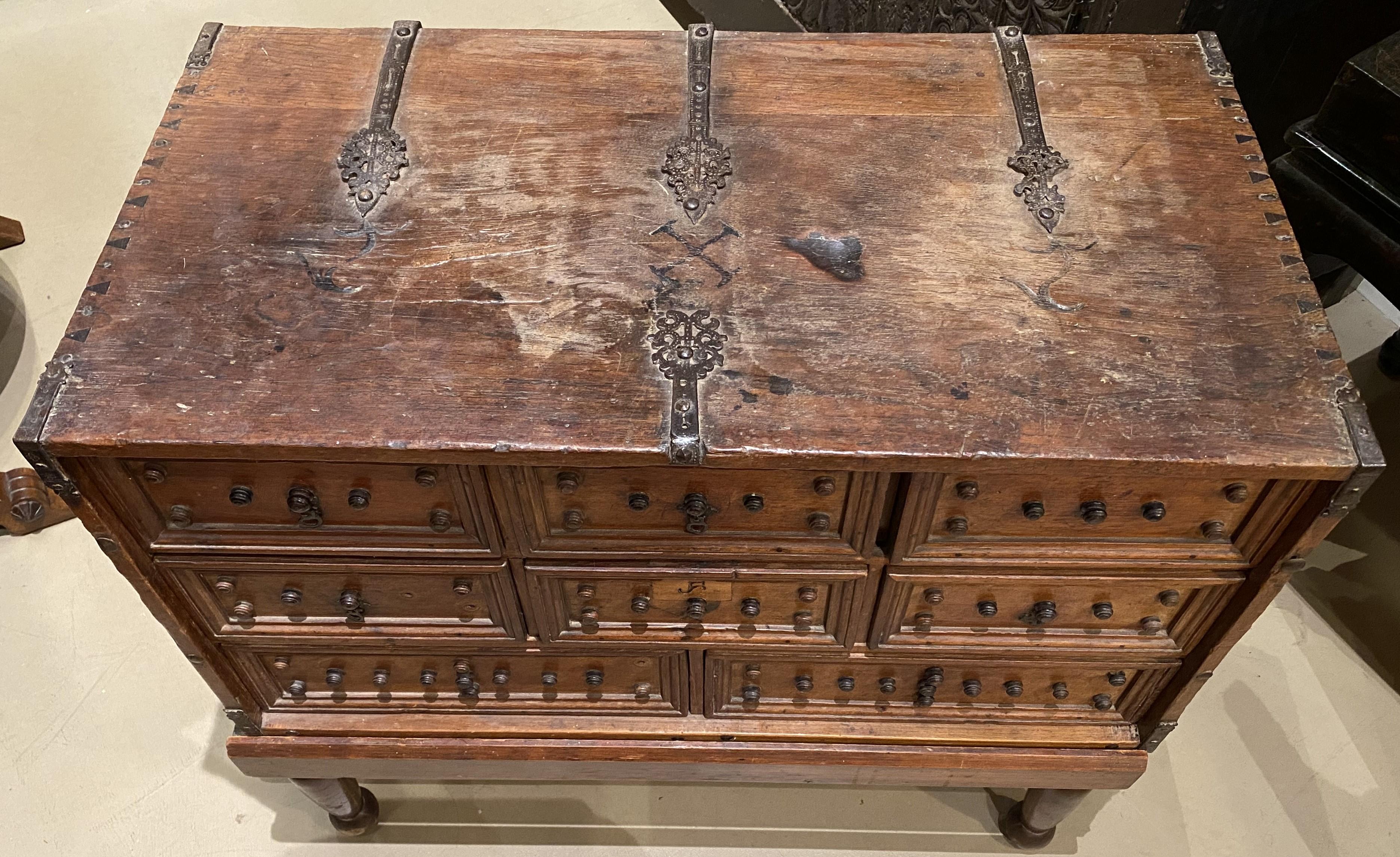 A fine example of a Spanish Baroque iron mounted oak vargueno or collector cabinet with eight drawers, beautifully detailed iron support straps and carvings on the top, forged iron handles, interesting wooden knob decoration on each drawer front,
