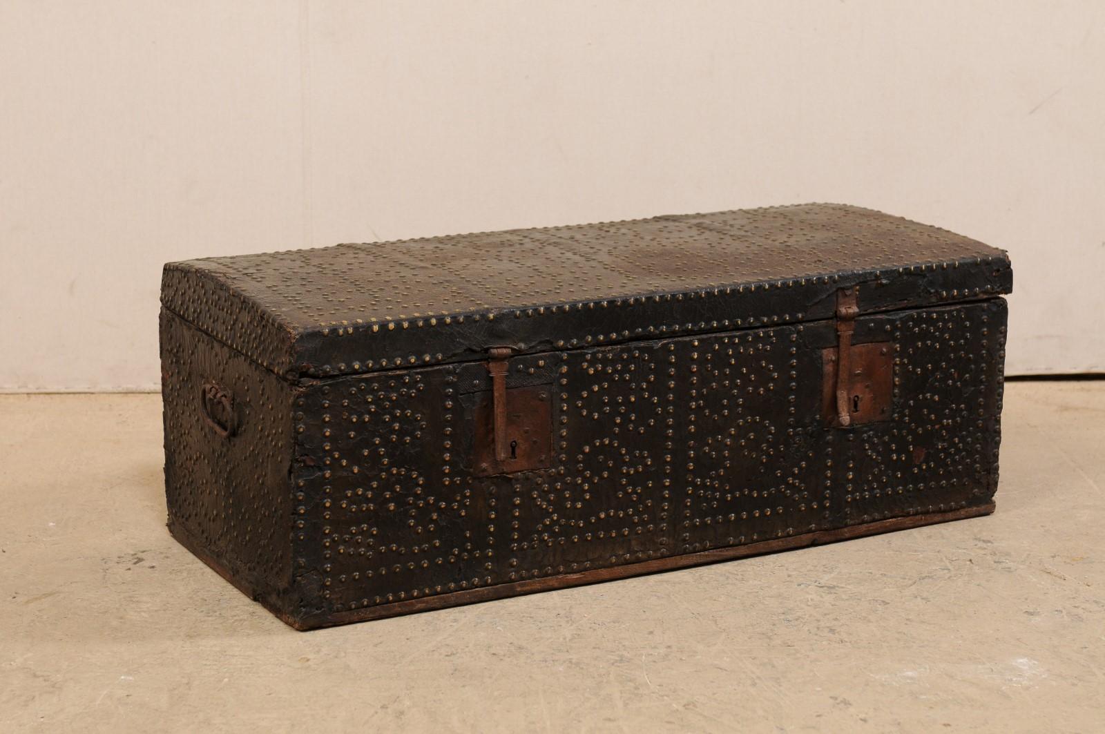 A Spanish Baroque leather-wrapped coffer brass accents from the 18th century. This antique Spanish coffer, with it's rectangular-shaped body, has been ornately decorated with nail head brass studs (which have a dark patina from age) along the top,