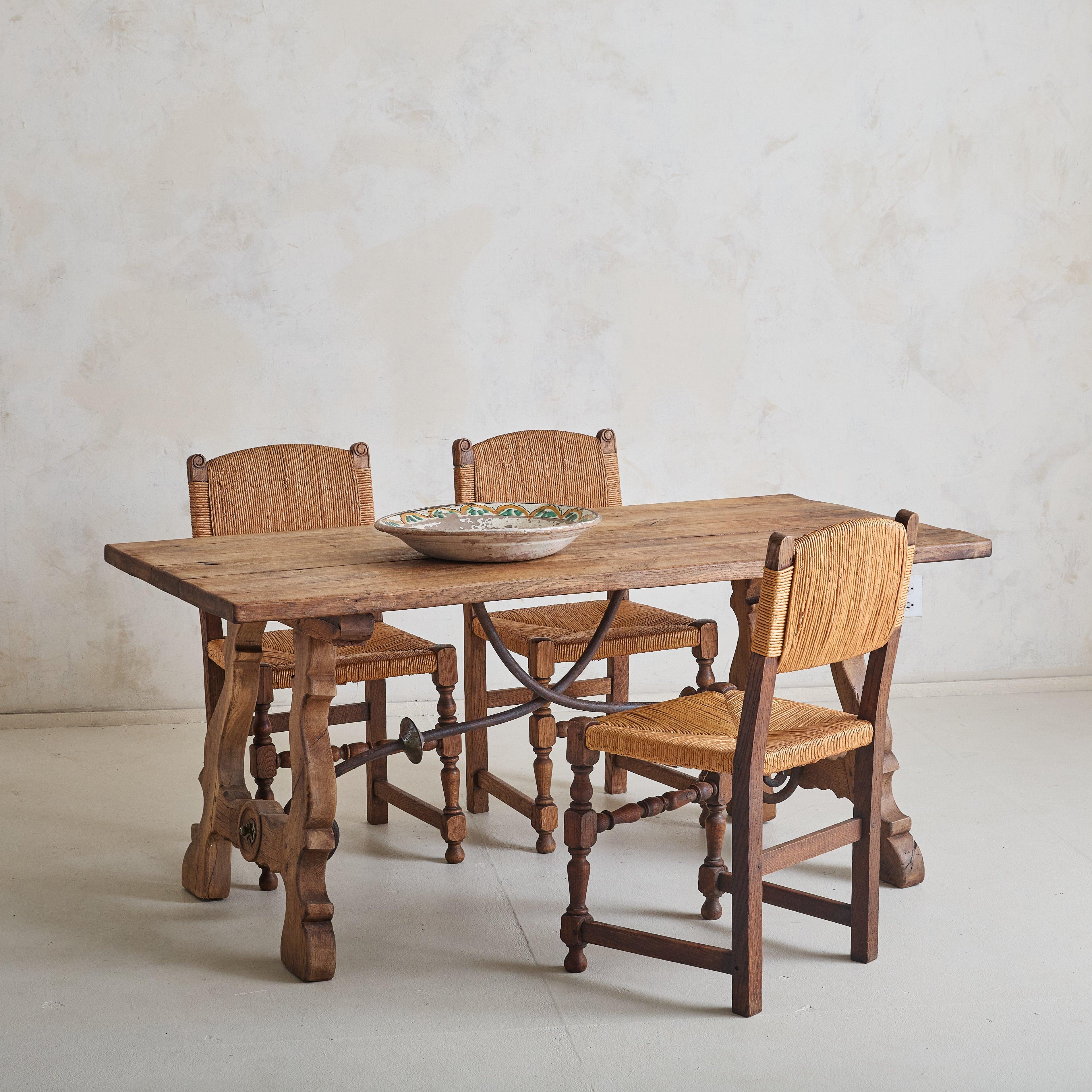 Made in Spain during the late 19th century, this antique dining table reflects the Spanish Baroque style. Crafted from solid oak, the table is defined by a rectangular plank top and gracefully carved lyre-shaped legs. Richly patinated wrought iron