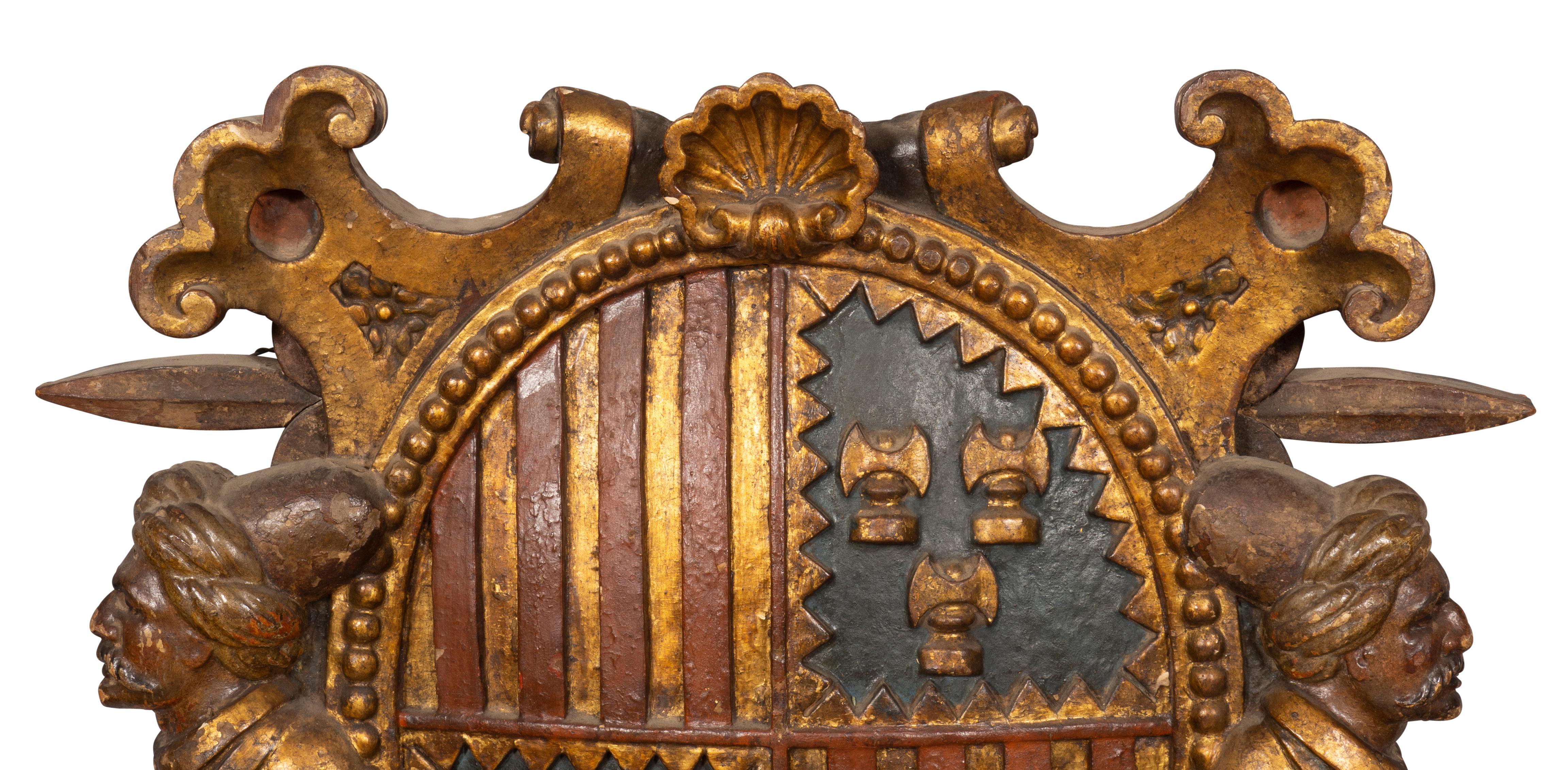 Oval shield with coat of arms and shell carving flanked by carved scrolls, the whole flanked by men with turbans , the base with the head of a soldier. This item is illustrated in 'Spanish Polychrome Sculpture in United States Collections