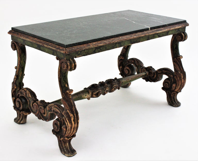 Elegant baroque style carved wood low table with dark green marble top. Spain, 19th century
The table stands up on two scrolled carved lyre legs adorned by acanthus leaves. They are connected by a carved wood stretcher. The marble top has beautiful