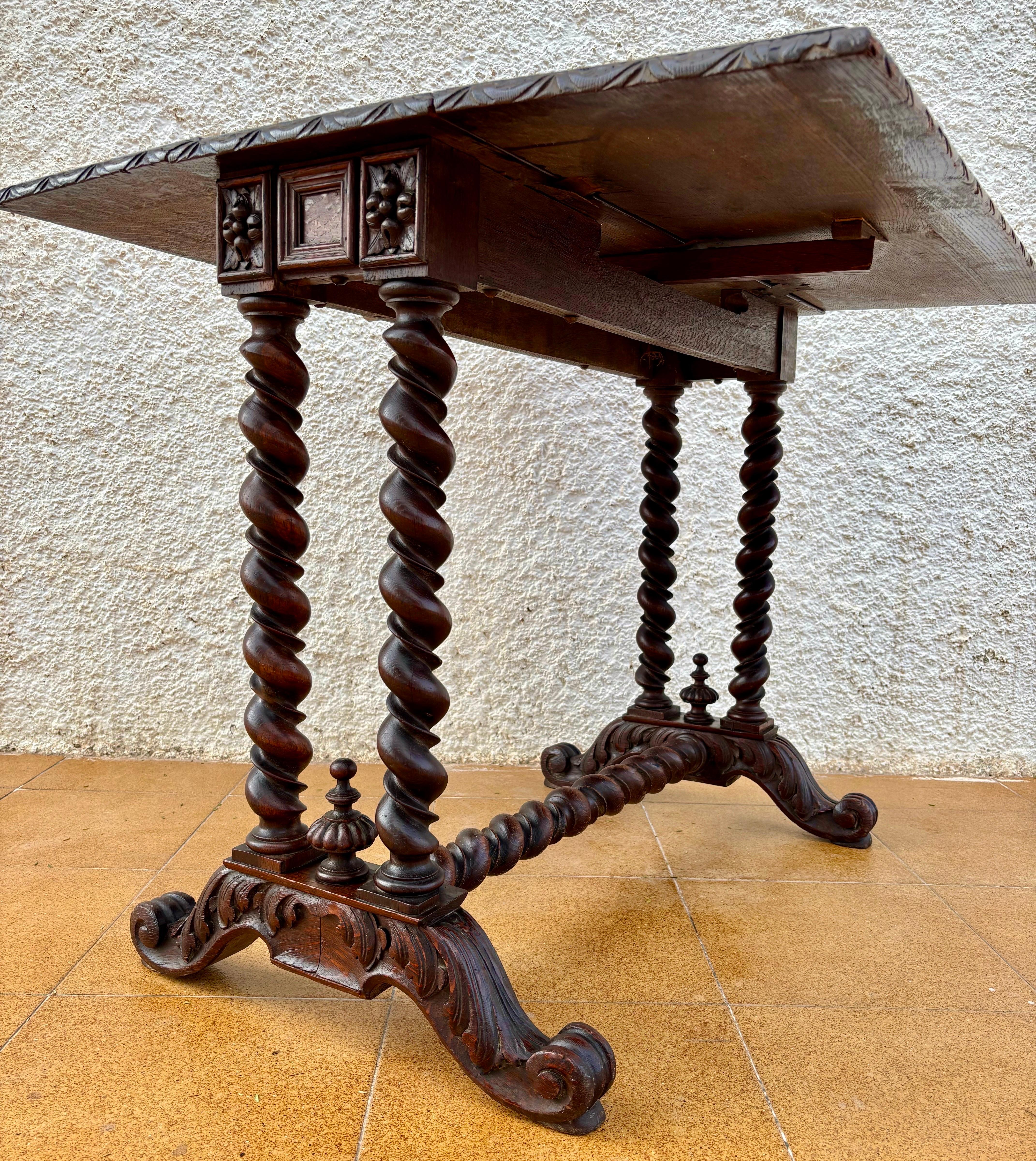 Rare Spanish Baroque Revival drop-leaf table with richly carved details, dating from the late 19th to early 20th century. The piece features a solid wood top with two folding leaves, supported by four stunning barley twist legs joined by an