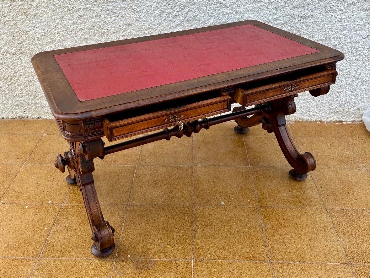 Magnificent Spanish Baroque Revival writing table dating from the late 19th to early 20th century, featuring an elegant leather-inset top framed by a richly carved wooden border. The frieze presents architectural carvings and decorative metal