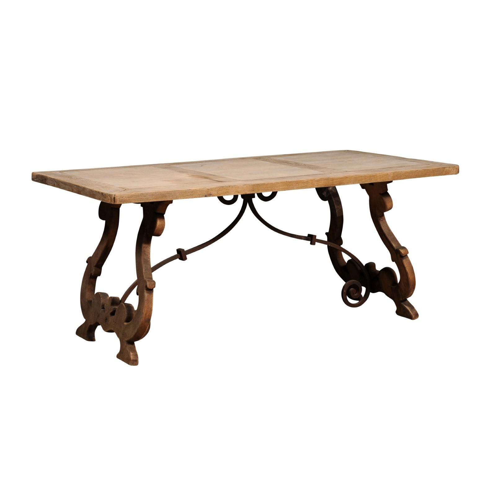 A Spanish Baroque style bleached oak Fratino table from circa 1900 with carved lyre-shaped legs and iron stretchers. Step back in time and embrace the captivating beauty of this Spanish Baroque style bleached oak Fratino table from circa 1900. Its