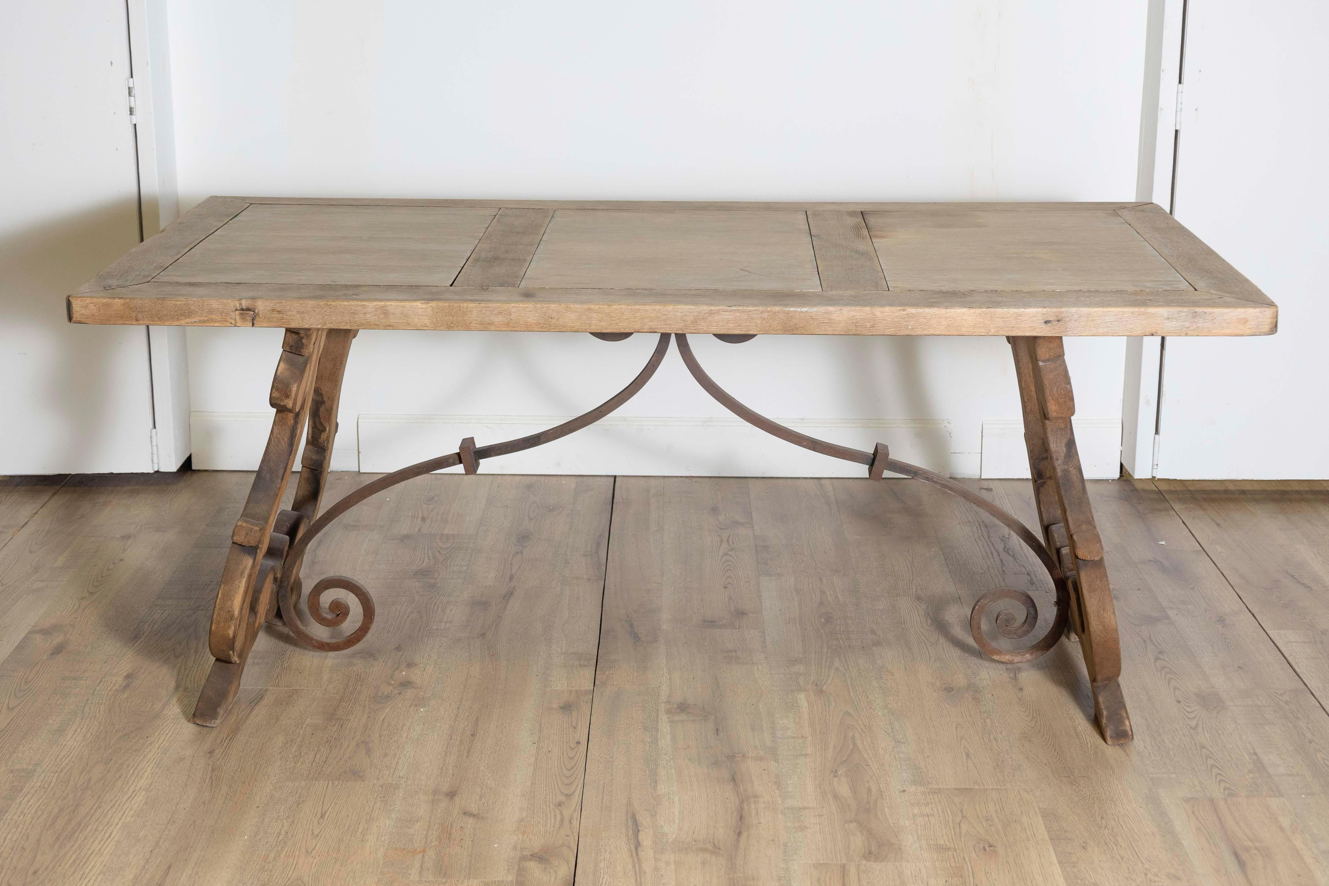 A Spanish Baroque style bleached oak Fratino table from circa 1900 with carved lyre-shaped legs and iron stretchers. Step back in time and embrace the captivating beauty of this Spanish Baroque style bleached oak Fratino table from circa 1900. Its