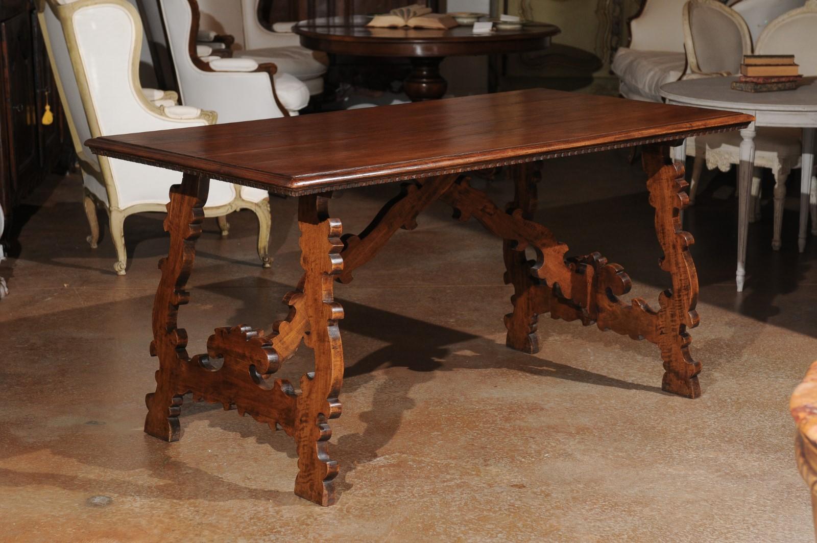 A Spanish Baroque style walnut Fratino table from the 19th century, with carved lyre-shaped legs. Created in Spain during the 19th century, this walnut table features a rectangular planked top adorned with discreet dentil molding on the lower edge,