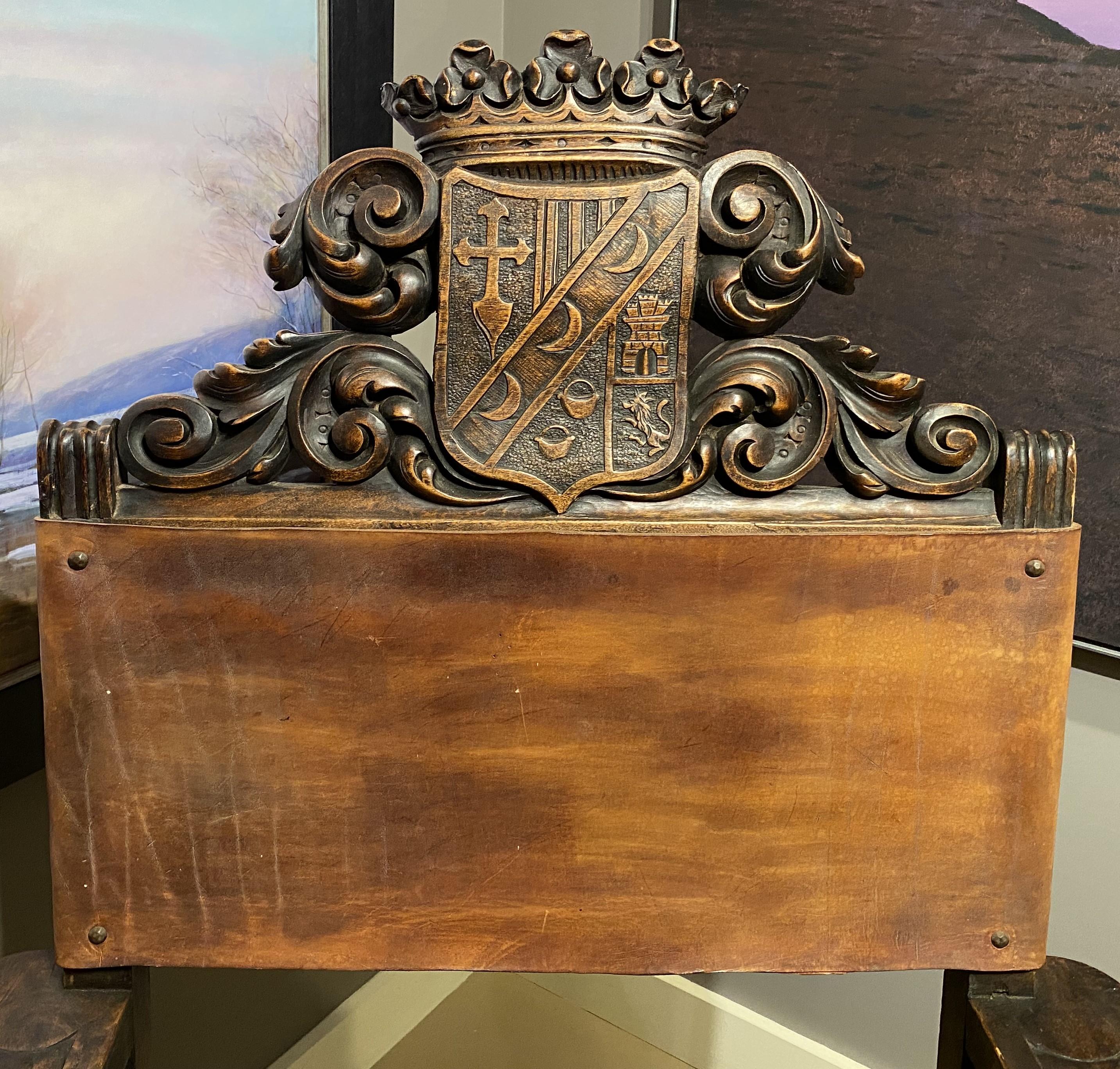 A nicely carved Spanish Baroque style carved oak armchair with detailed scroll carved crest, decorative arms, carved corner figures, foliate carved front stretcher, Spanish feet, and leather seat with large patinated rosette upholstery nails. Dates