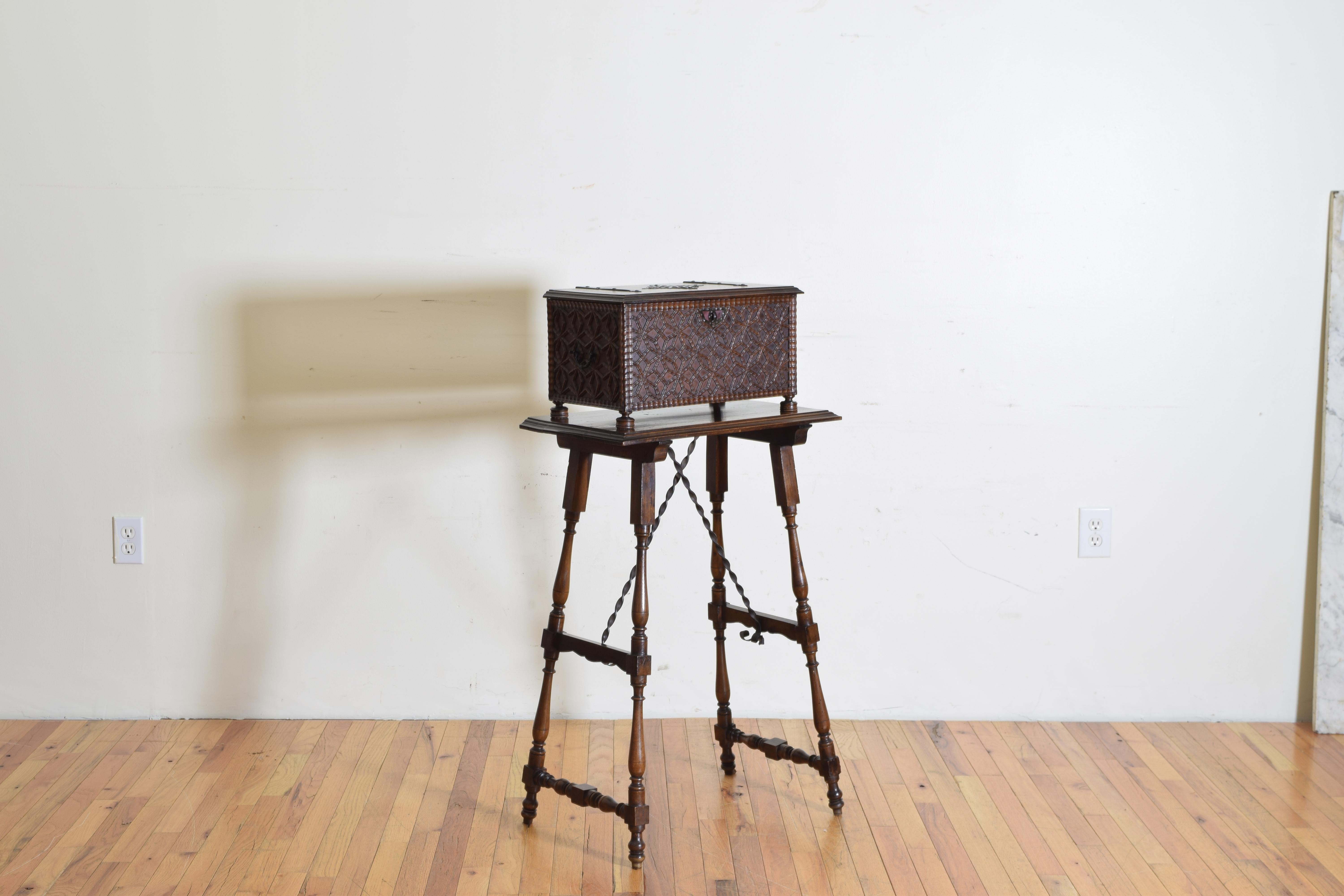 The box with intricate applied carvings and a gadrooned carved molded edge with iron hinges and a centered medallion raised on round flattened disk feet, the tall stand with turned legs joined by wooden and iron stretchers, first quarter of the 20th