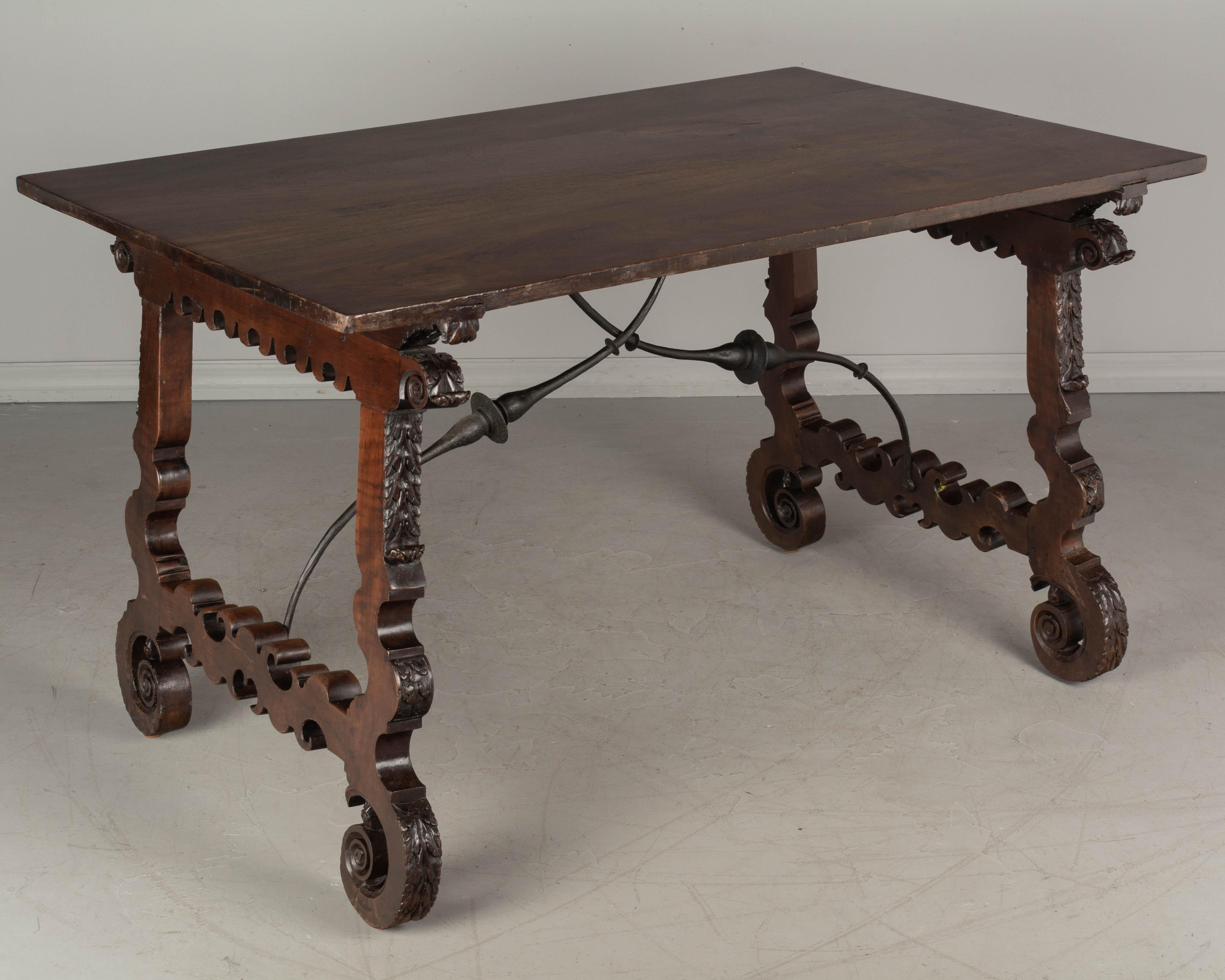 A Spanish Baroque style center table made of solid walnut with lyre shaped legs joined by forged iron stretchers. The top is made has a beautifully patterned wood grain and is made from book matched veneer of walnut. The legs have elaborate cut-out